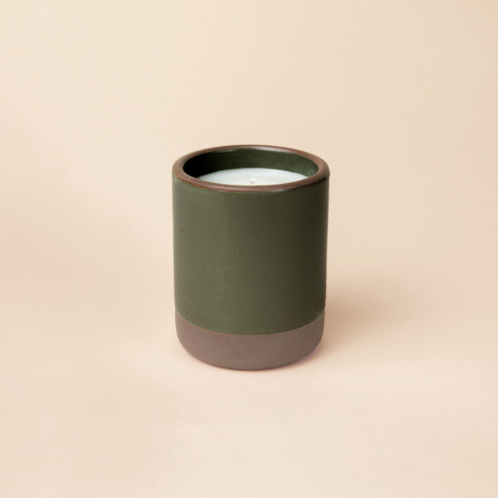 A candle in a large ceramic vessel dipped in a dark forest green color.