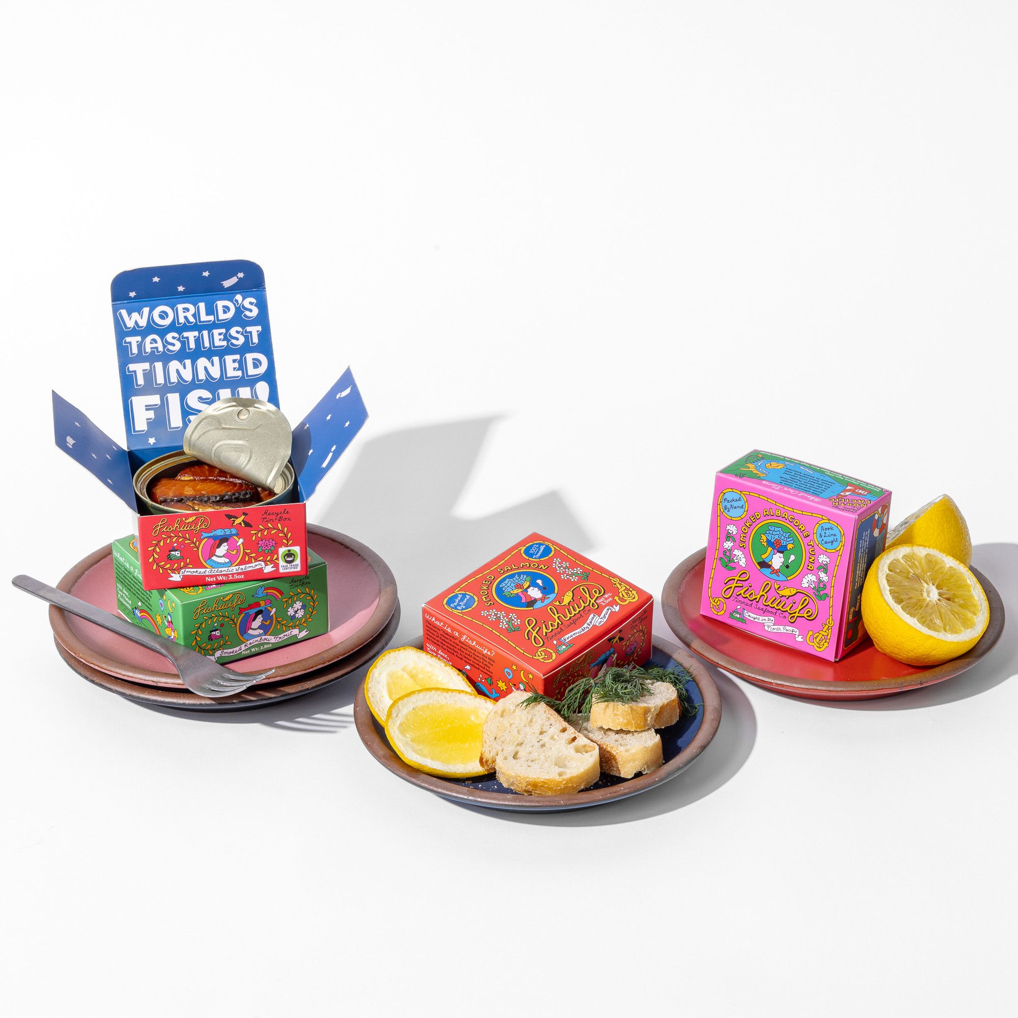 3 plates nestled together with boxes of tinned fish and accompaning lemon slices and sliced bread.