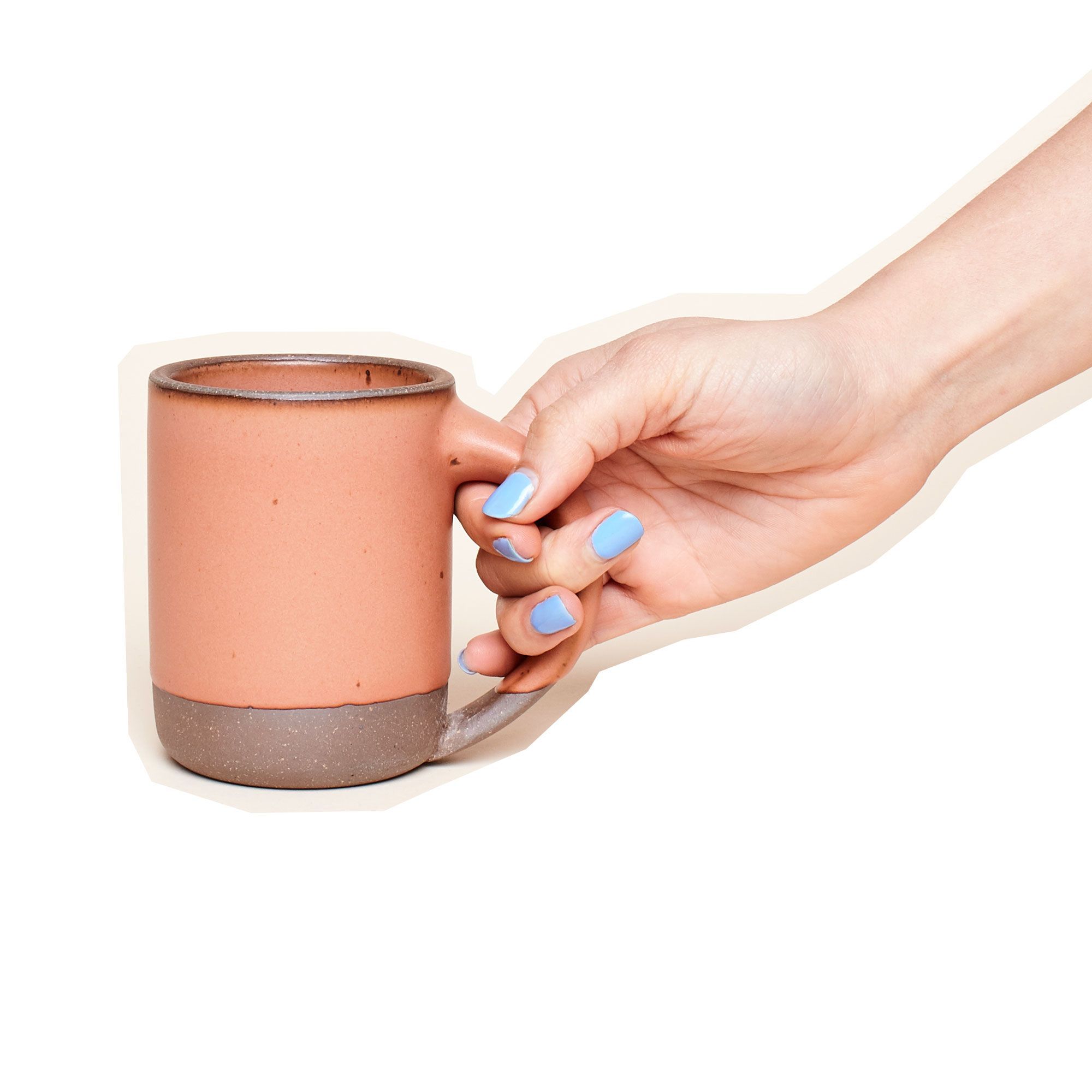A hand holds an East Fork Mug in a warm peach color with an unglazed rim and bottom