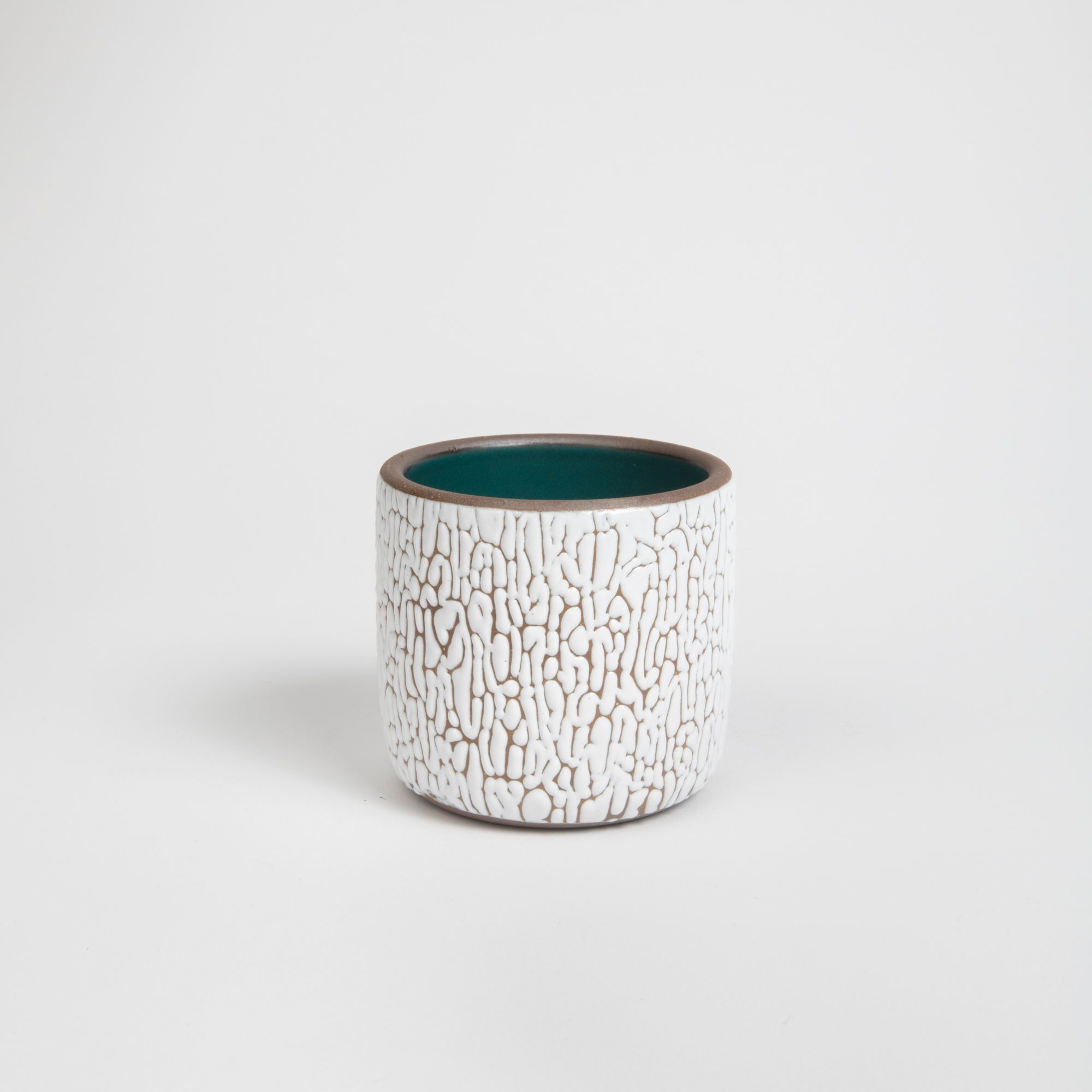 A short white ceramic vessel with cracked texture and the interior being dark teal