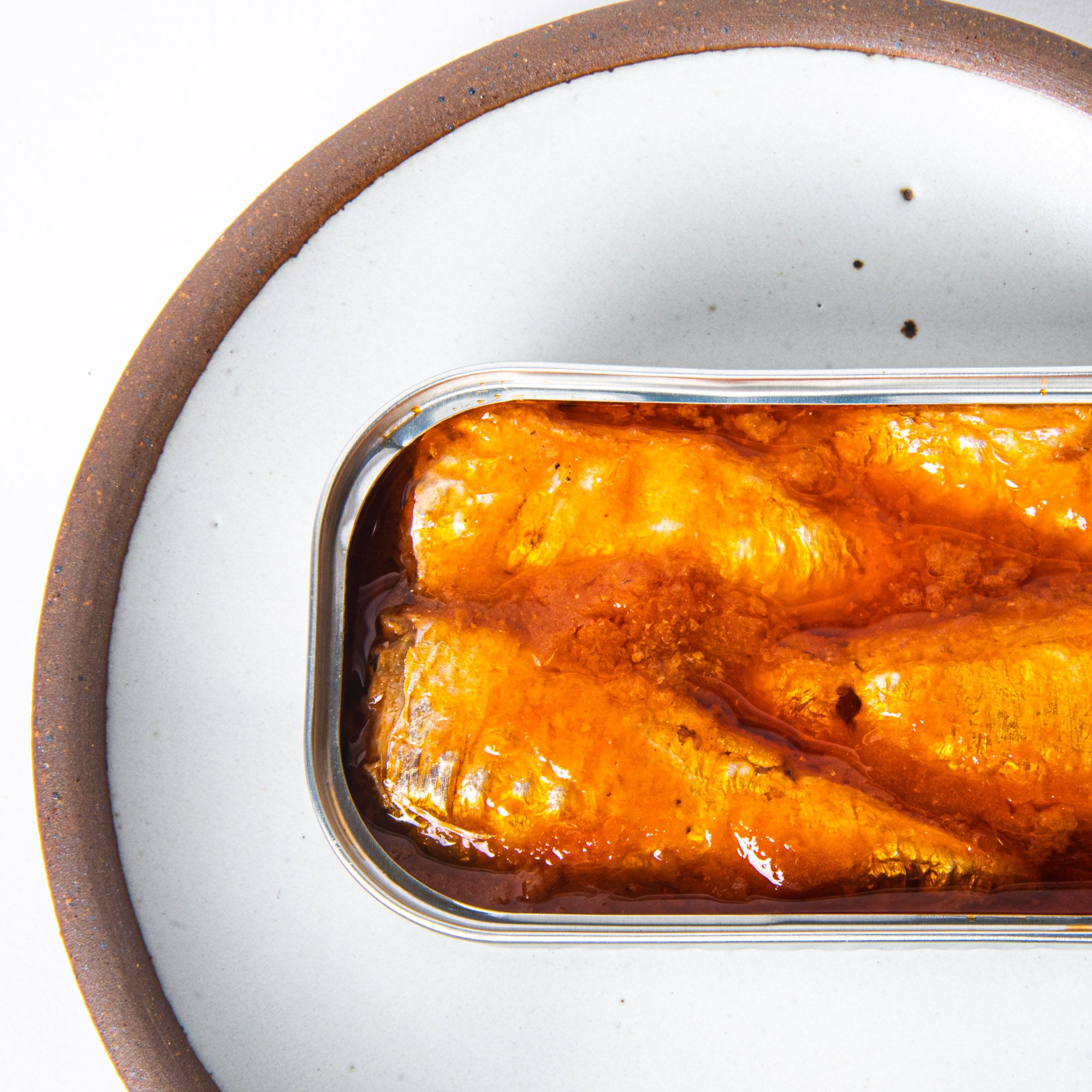 Tin of sardines in tomato sauce opened on a white plate