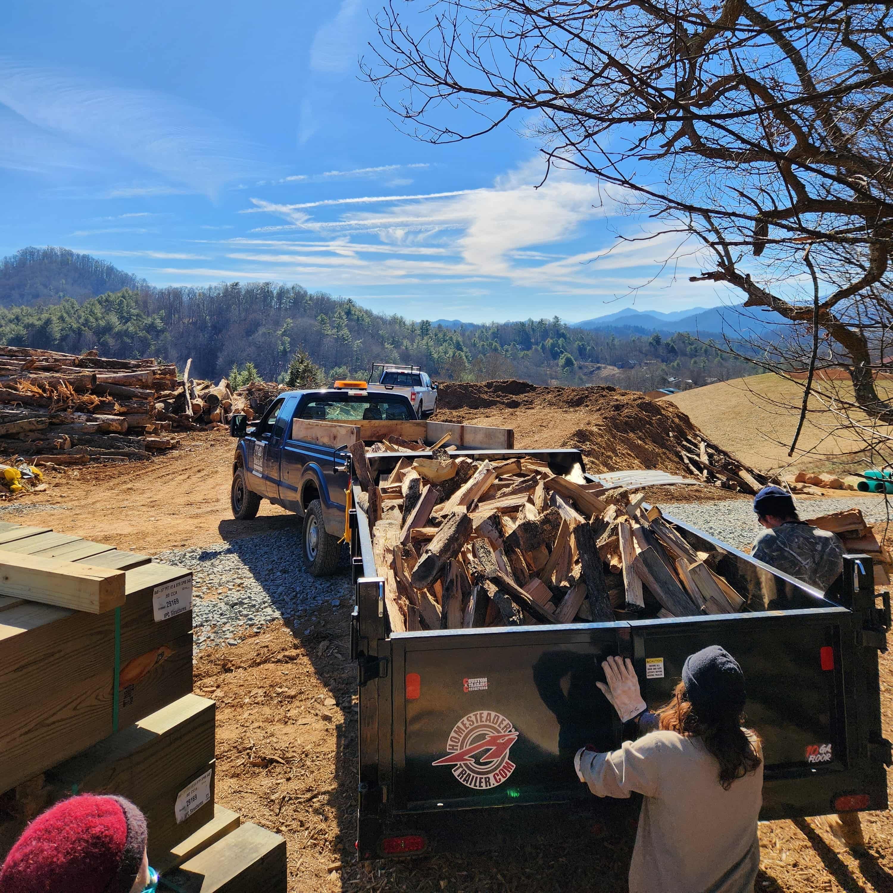 Outside, a truck and trailer are filled with chopped wood from the area.