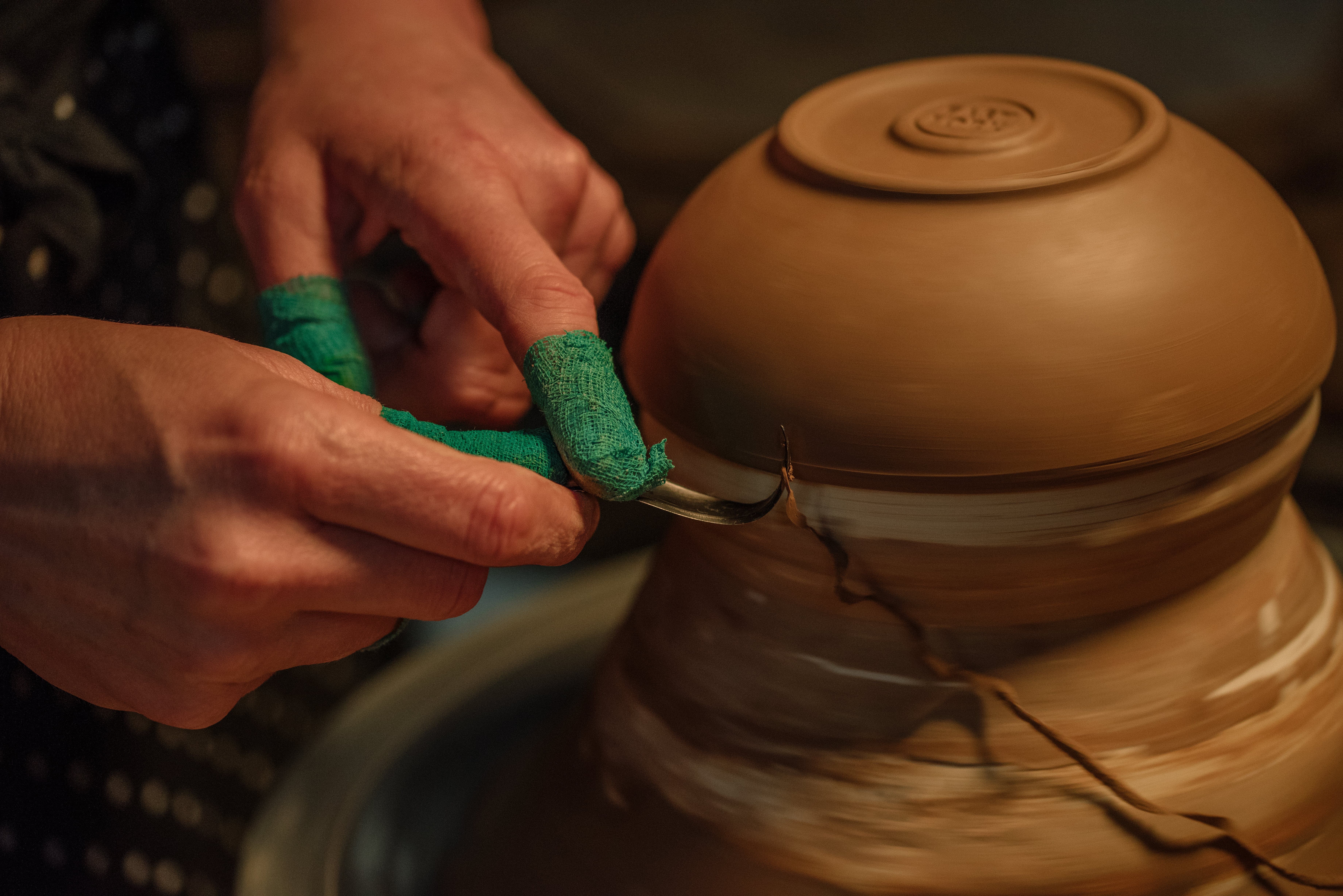 Hands trimming edges of pottery bowl
