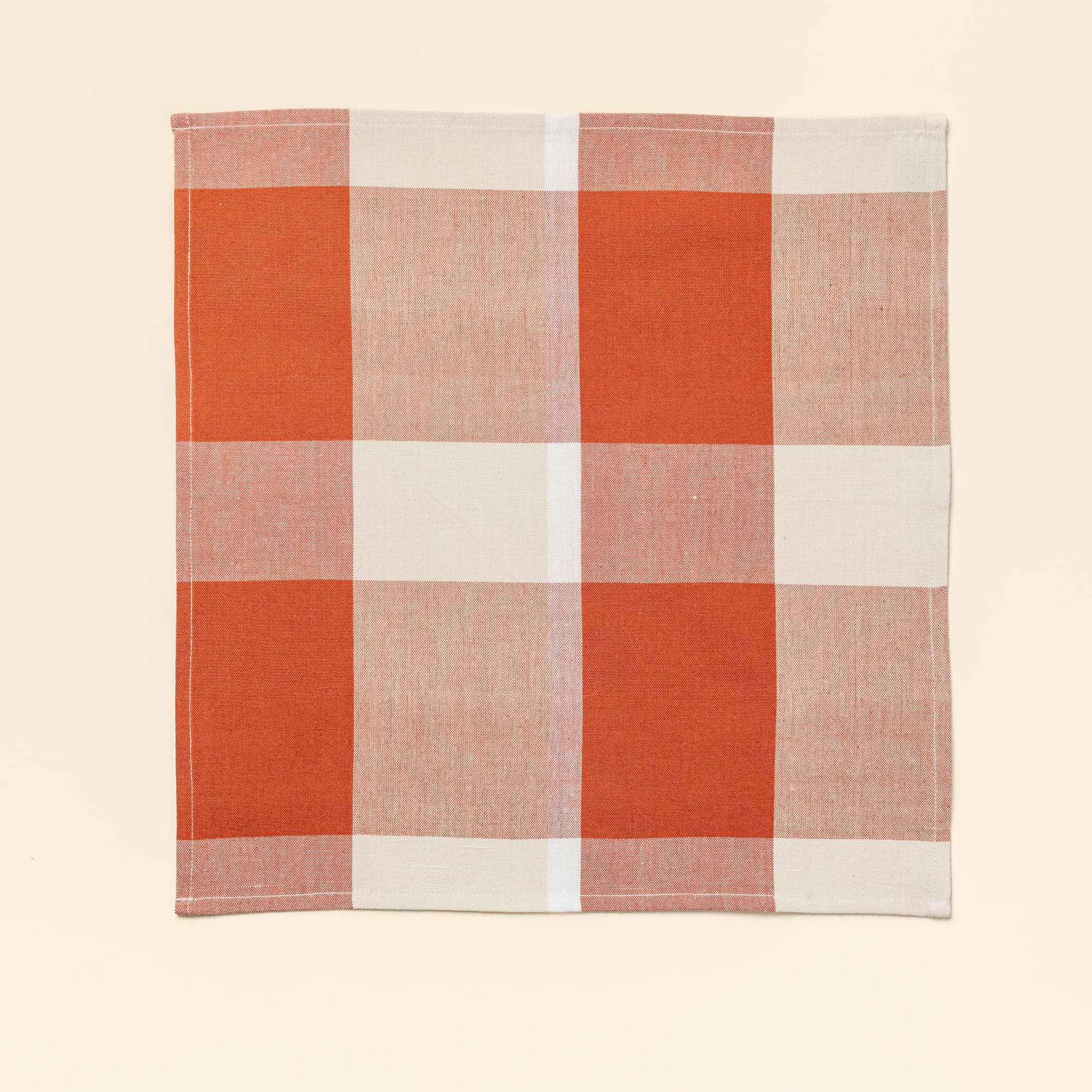 A flat square dinner napkin in a rust and cream gingham pattern.