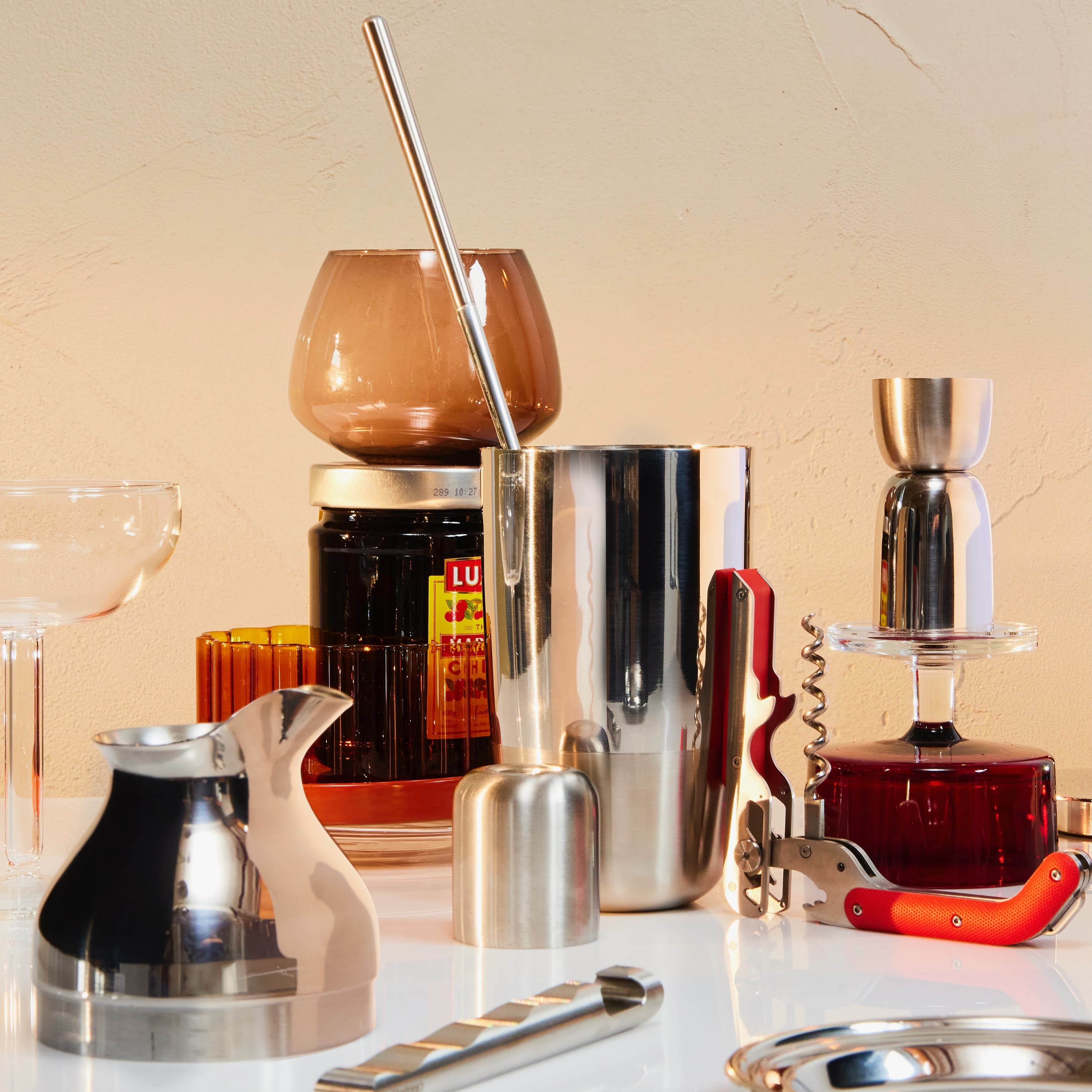 An artful assortment of the Mescola Cocktail Set with other accessories, glassware, and a jar of cherries.