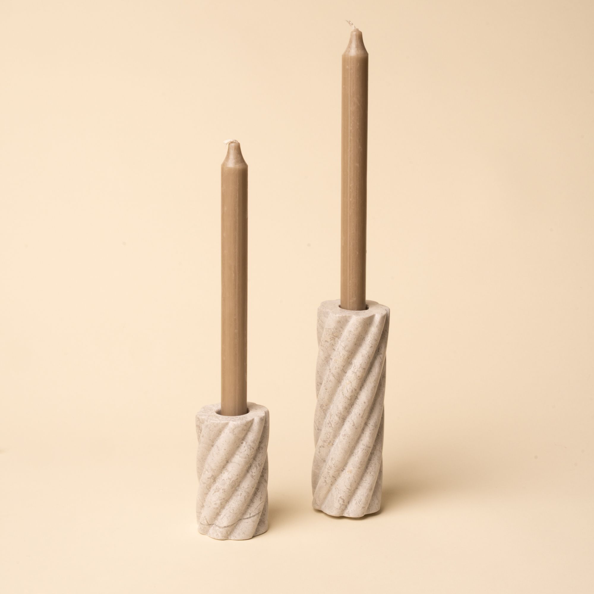 Pair of spiral-carved stone candle holders with taper candles, one taller and one shorter, against a neutral background.
