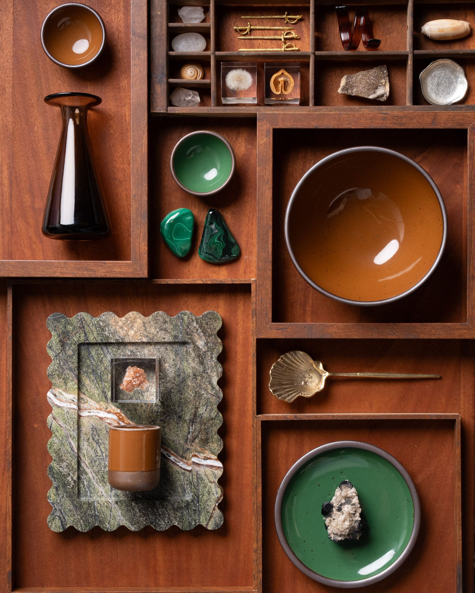 Wooden display with glossy green and brown ceramic bowls, malachite stones, crystals, shells, and decorative objects.