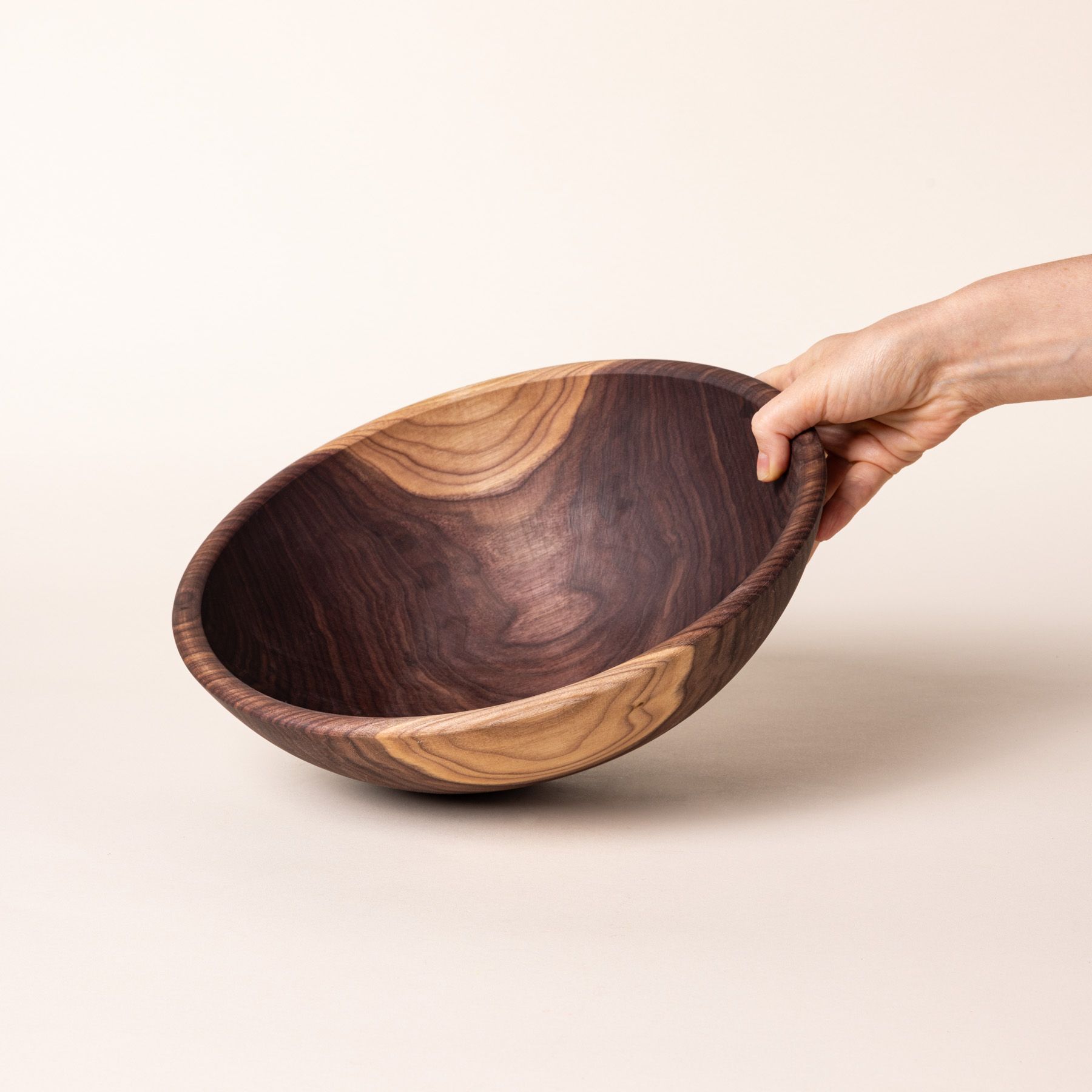 A hand holds out a large walnut wood bowl