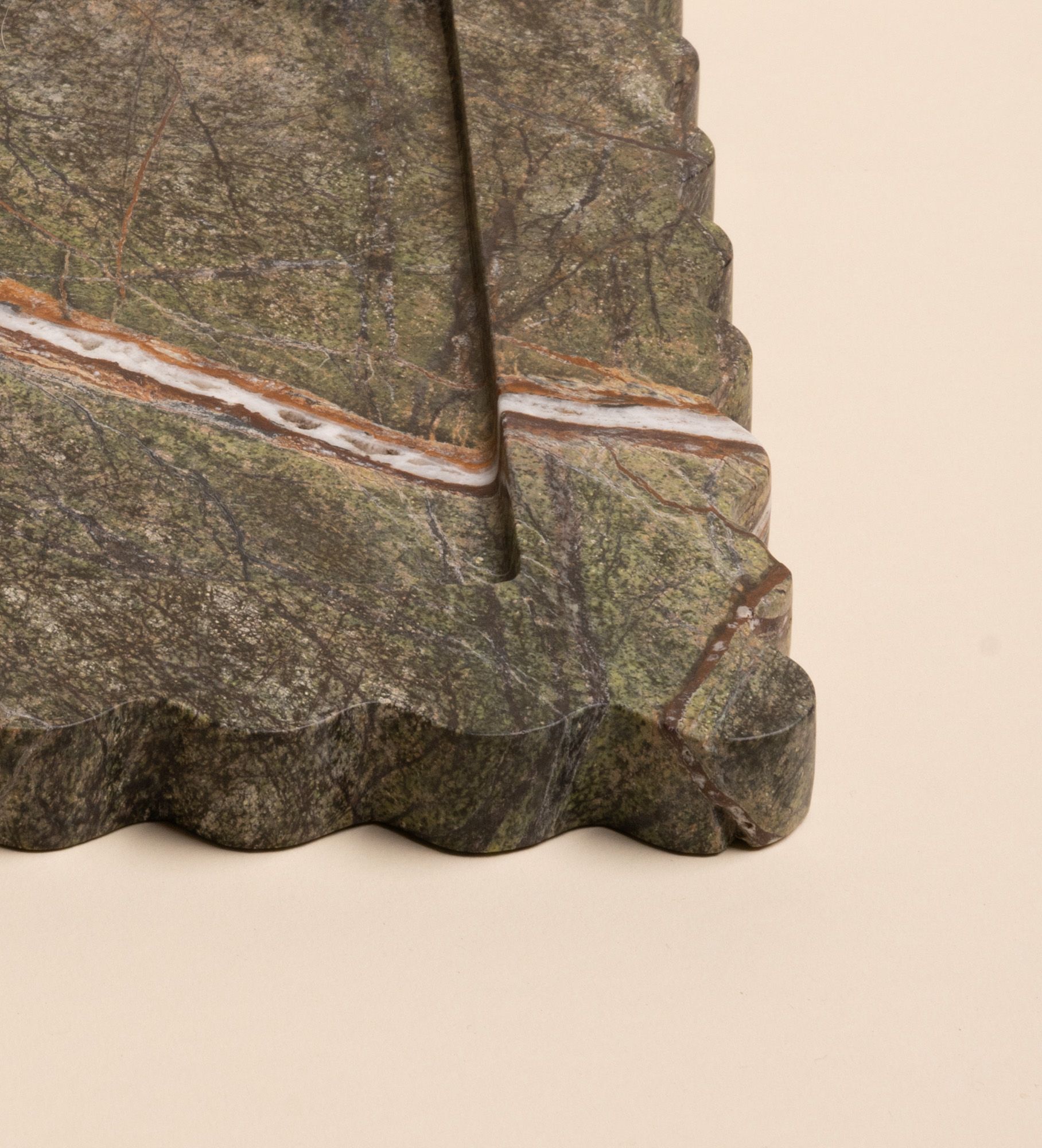 Closeup of a corner of a rectangular green marble tray with scalloped edges and a bold diagonal vein of white and rust running across its surface.
