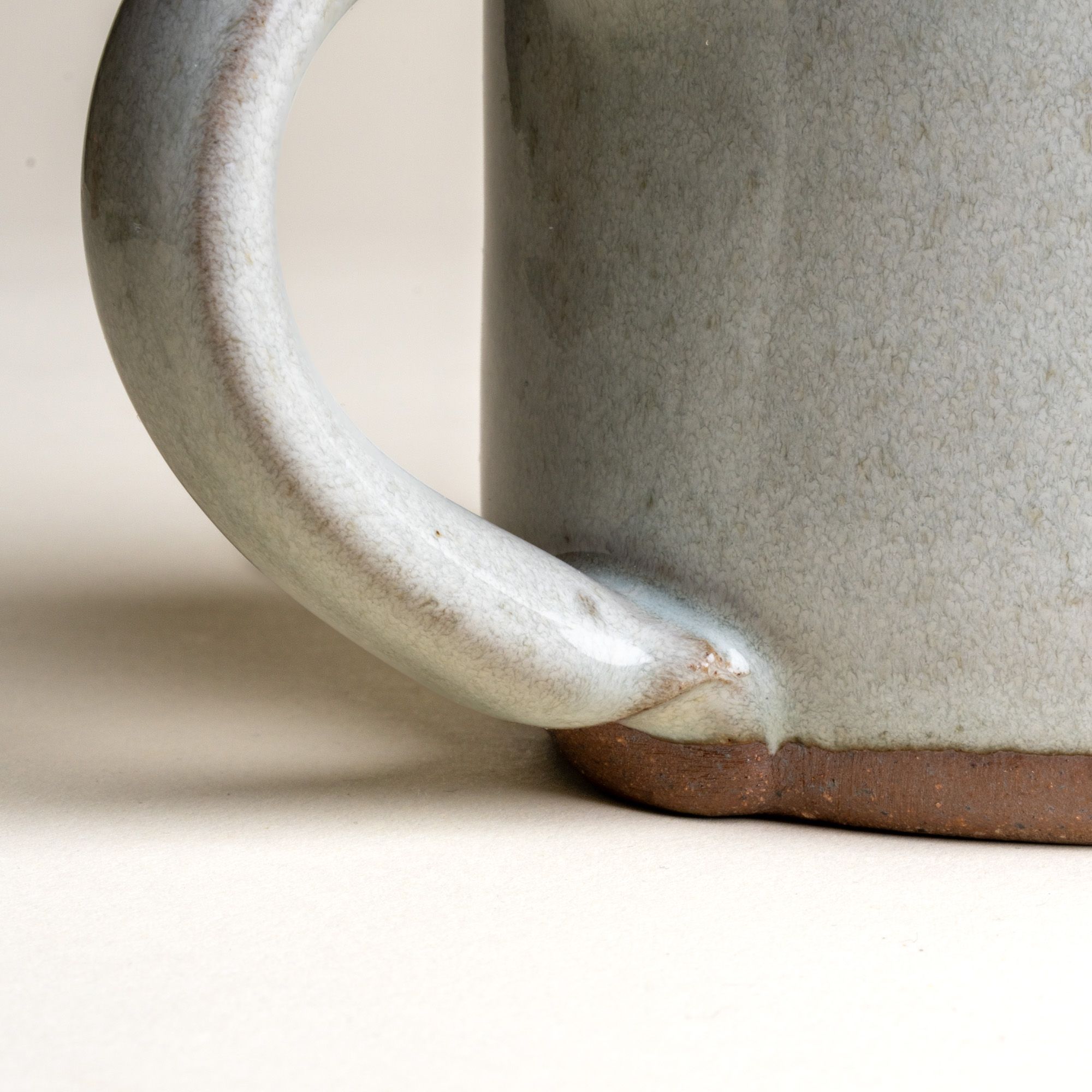 A close up of a handle on a medium sized ceramic mug with handle in a reactive icy white color featuring iron speckles