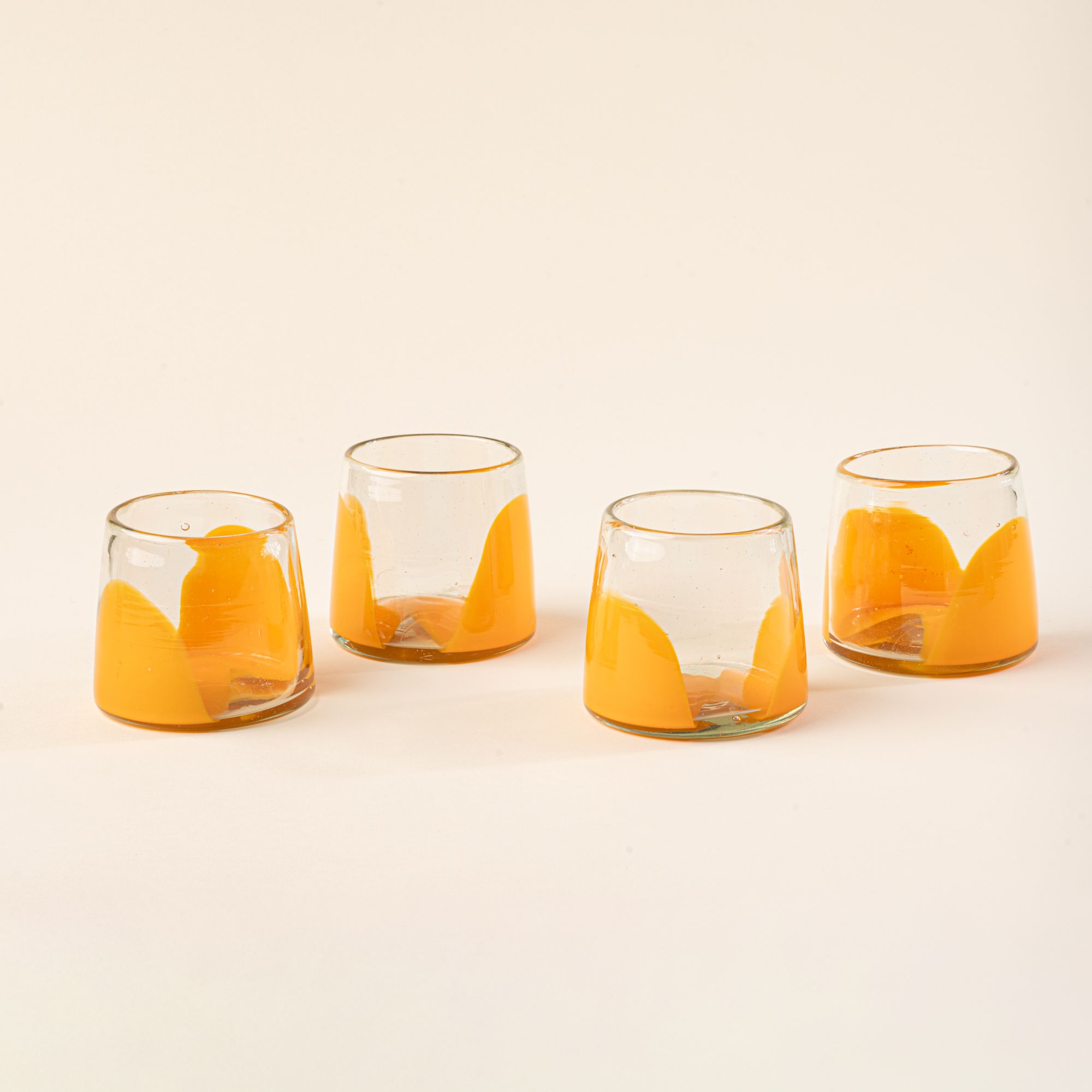 Four short clear glasses with orange arch bases arranged in a row on a light background.