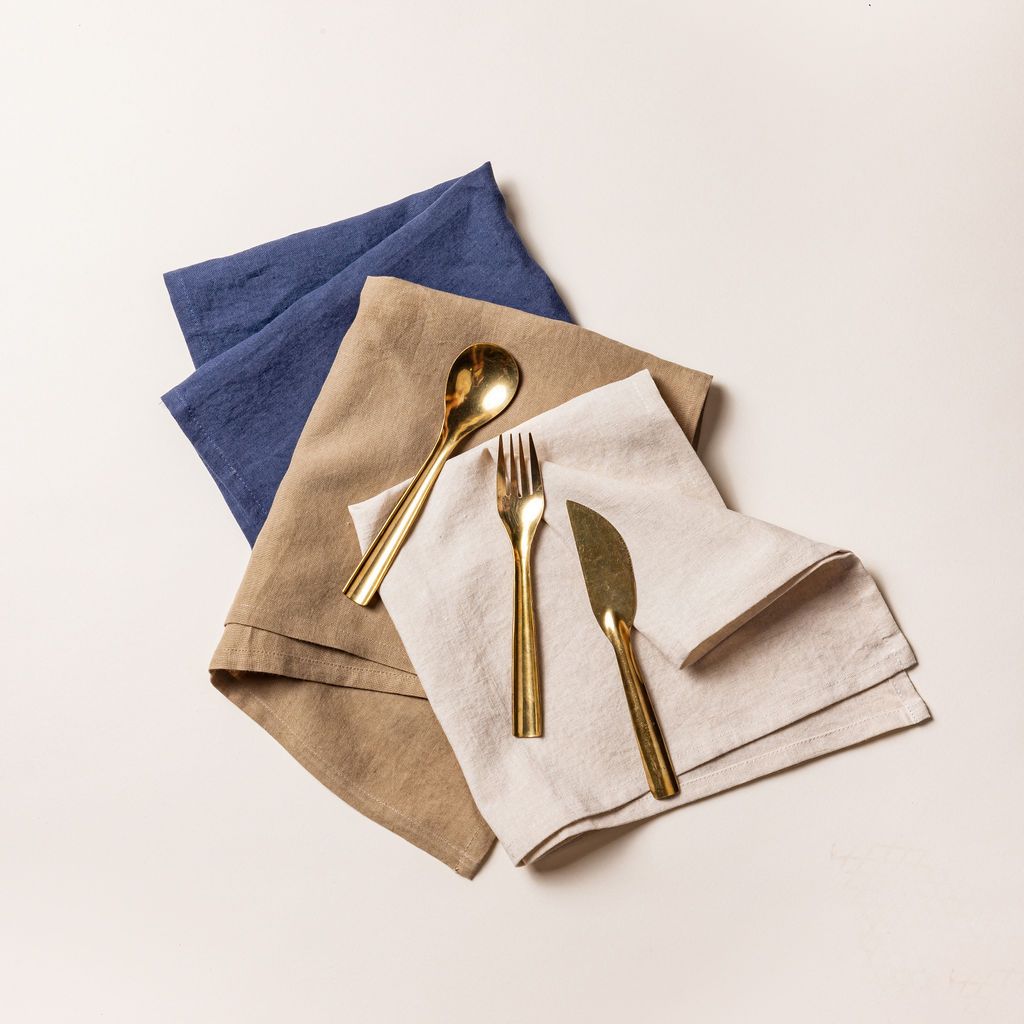 A shiny brass fork, knife and spoon sitting on folded linen napkins in muted blue, natural, and cream colors.