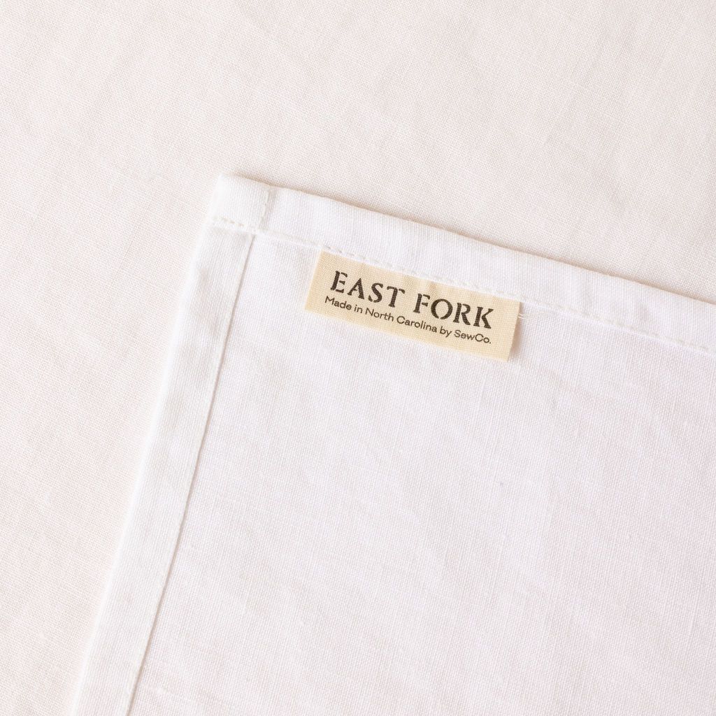 A white linen napkin close up of texture and sewn-in corner tag that reads "East Fork"