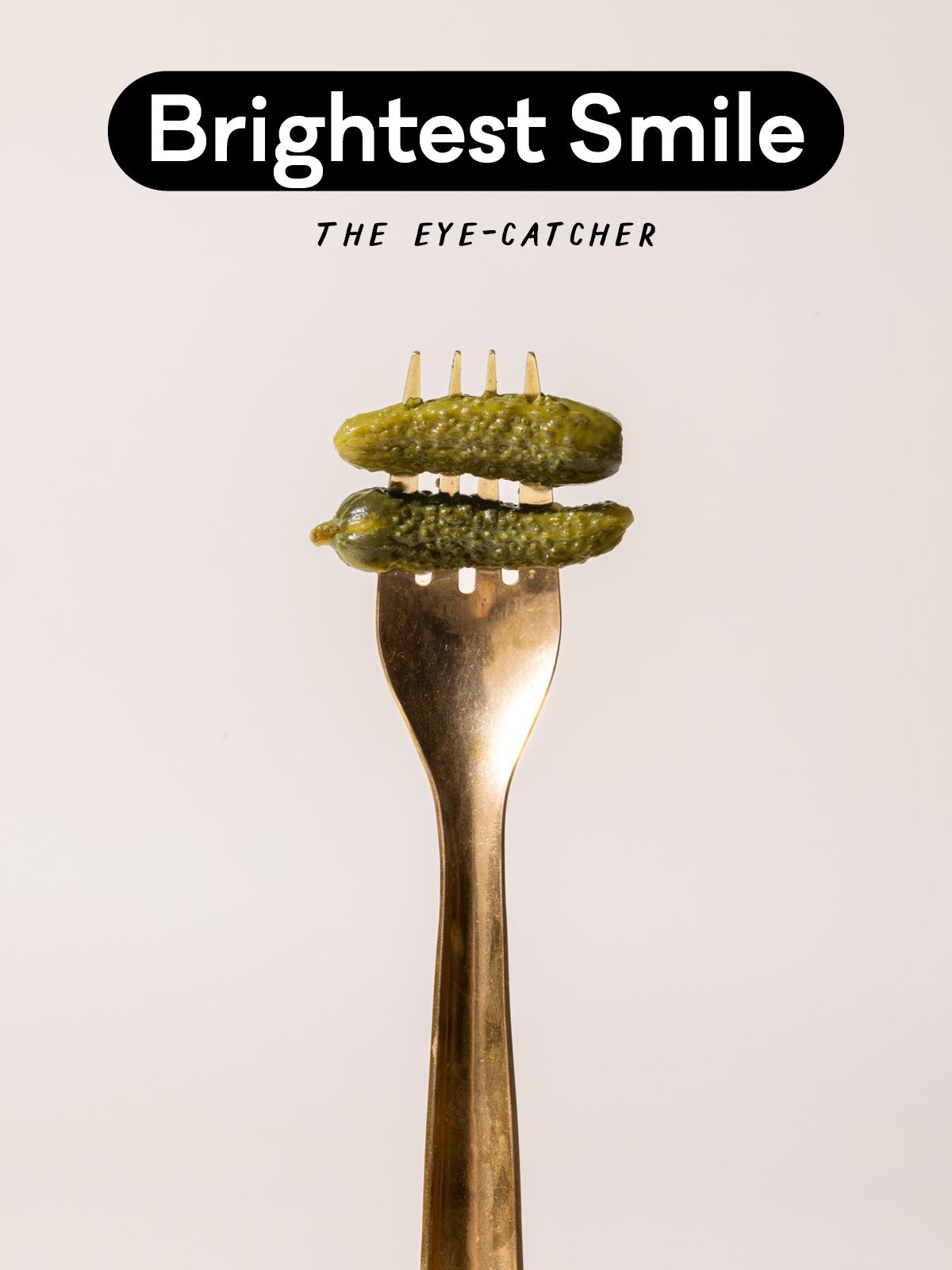 A brass fork with small pickles on the prongs and text that reads "Brightest Smile - The Eye Catcher"