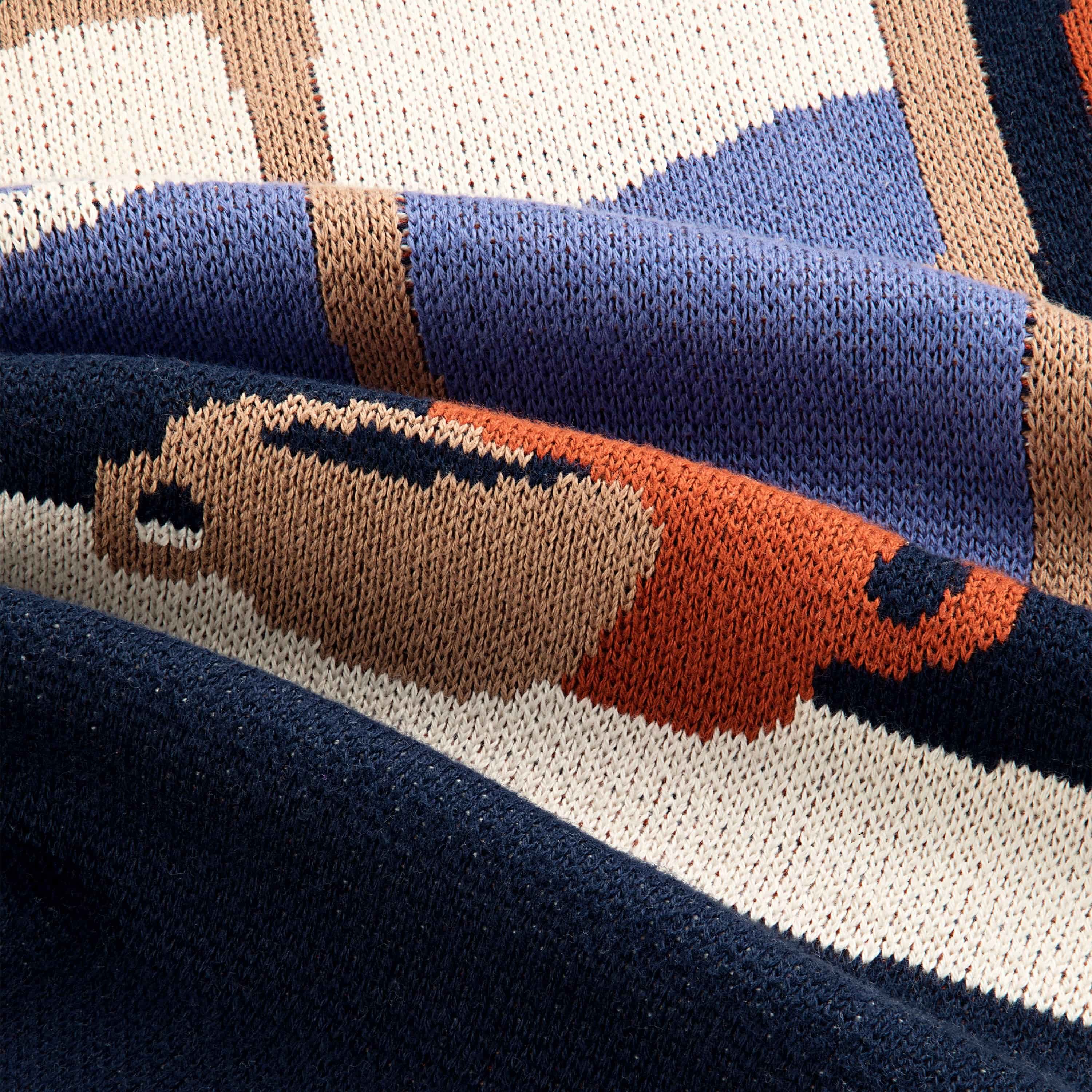 A closeup of a sweater with an illustration of a pottery workshop with a large window, shelves, and table with mugs and bowls. The sweater features cream, navy, terracotta, tan and blue colors.