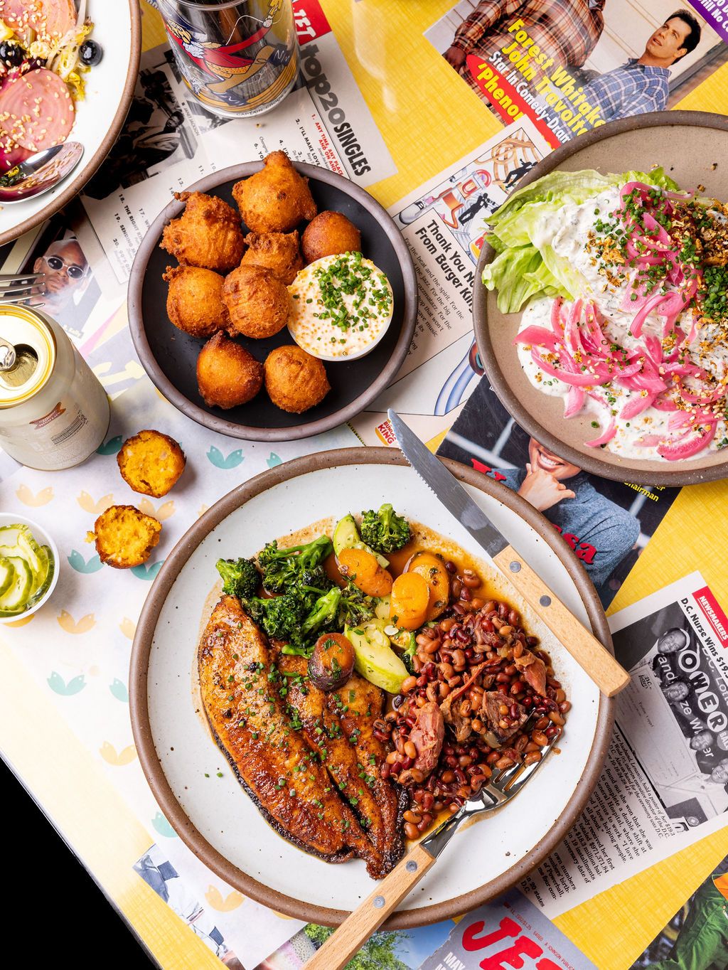 Multiple ceramic plates filled with foods like fish, hushpuppies, veggies and more.