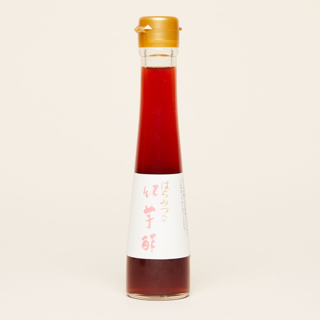 A tall bottle that flares toward the base filled with purple sweet potato vinegar and a gold top