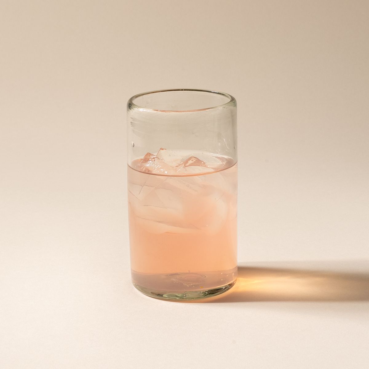 A tall clear drinking glass filled with pink lemonade.
