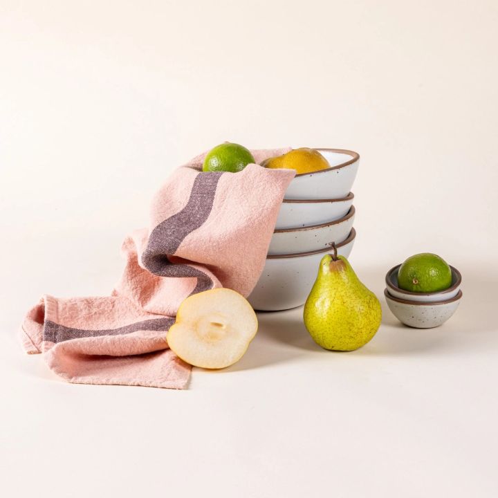 A salmon linen towel with a stack of white ceramic bowls, and various fruits