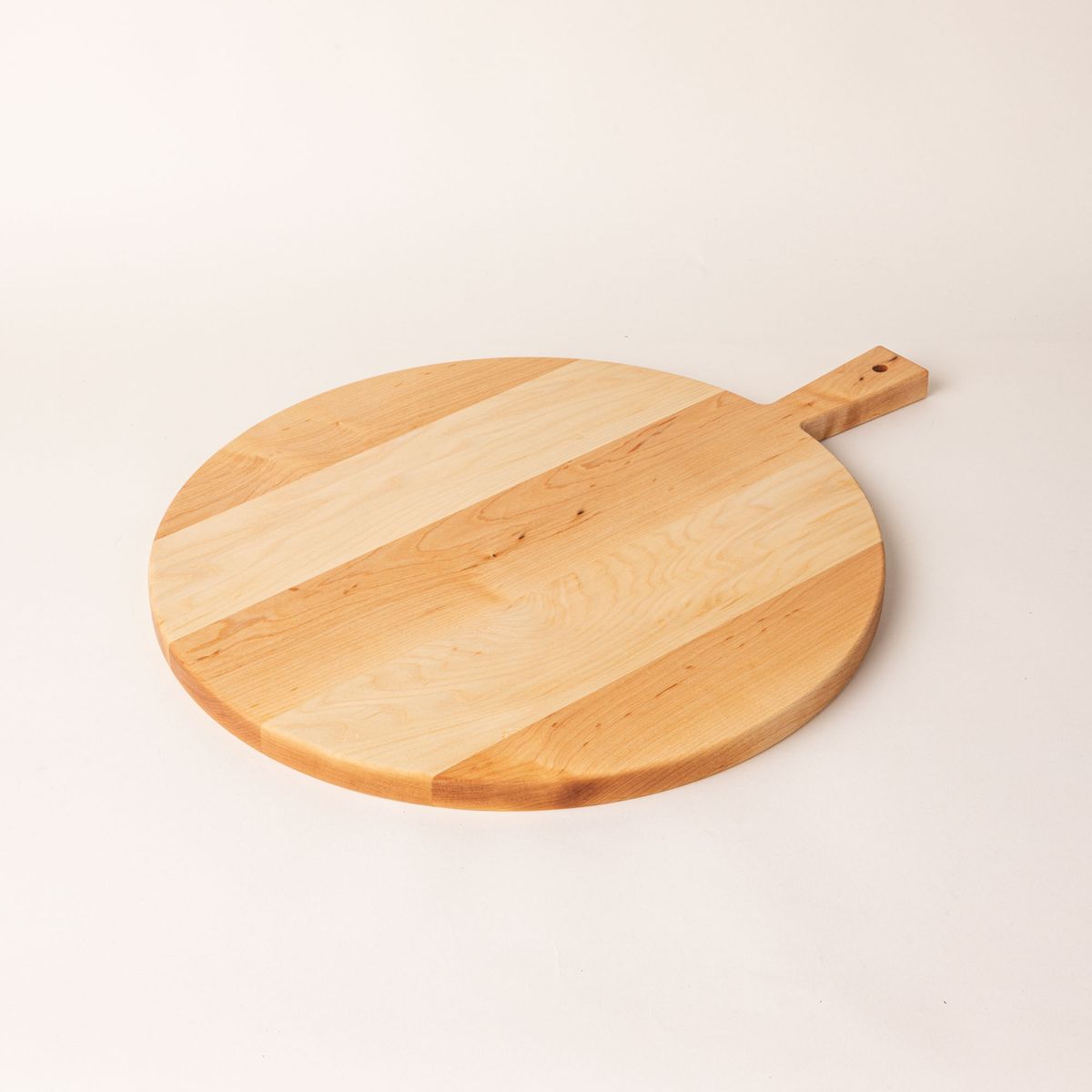 A round wooden serving board with a short rectangular handle with a hole for hanging