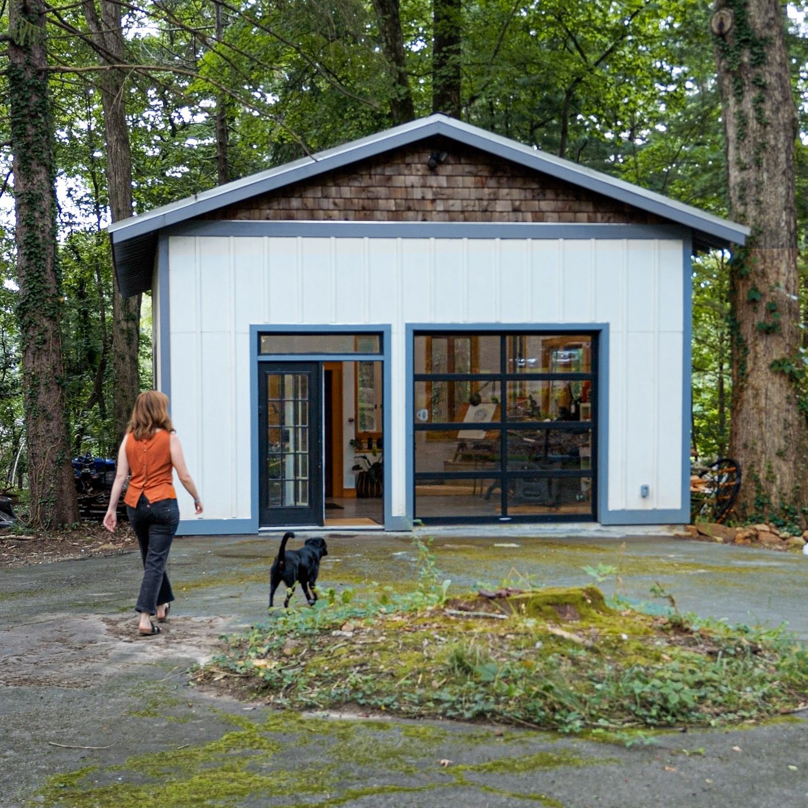 Outside, Nicole and her dog walk to her studio which is a stand alone white building with large windows and door.