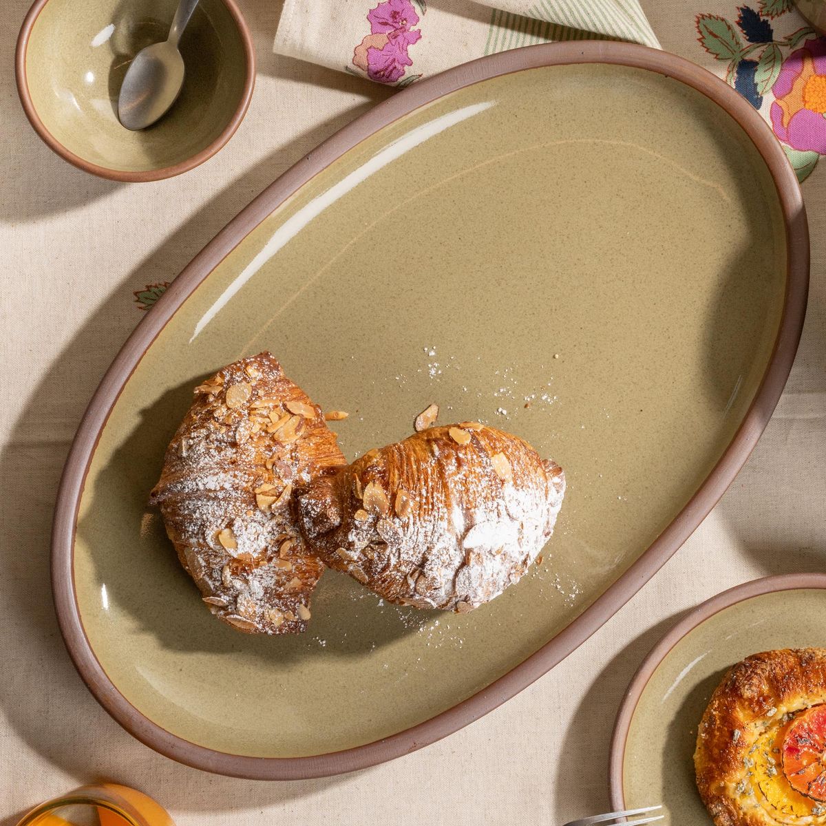 Reflective dappled grey-green oval stoneware platter with almond croissants dusted in powdered sugar.