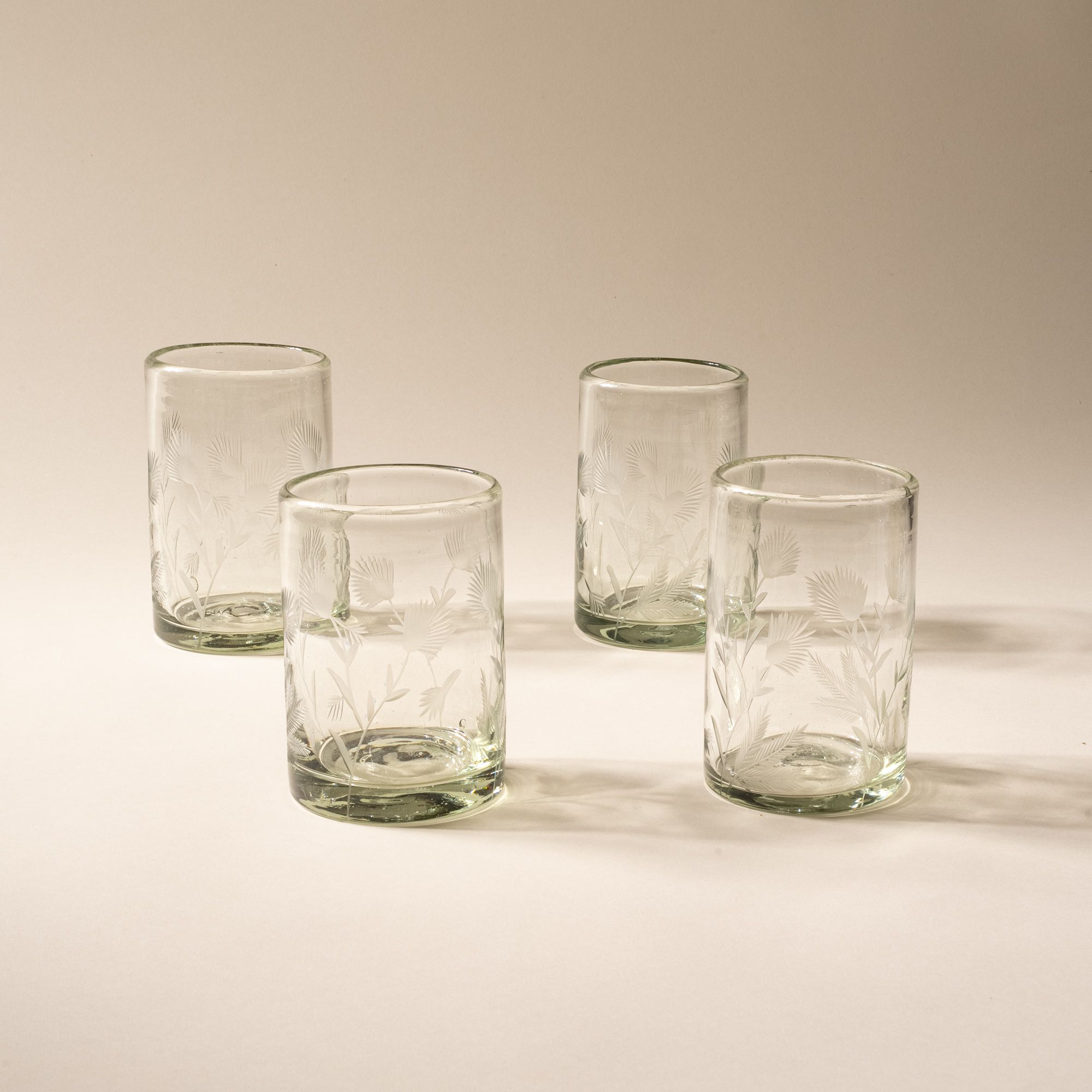 Four clear tumbler glasses made of recycled glass with etched thistle designs on it