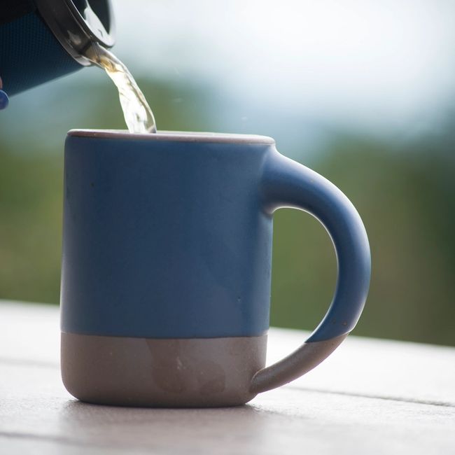 The East Fork Mug in Blue Ridge, a stately, denim-colored glaze, sits atop a picnic table, with tea getting poured into it.