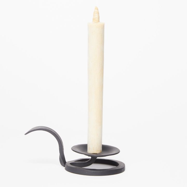 A black cast iron candle holder with a circular base containing a tall cream candle on a white background
