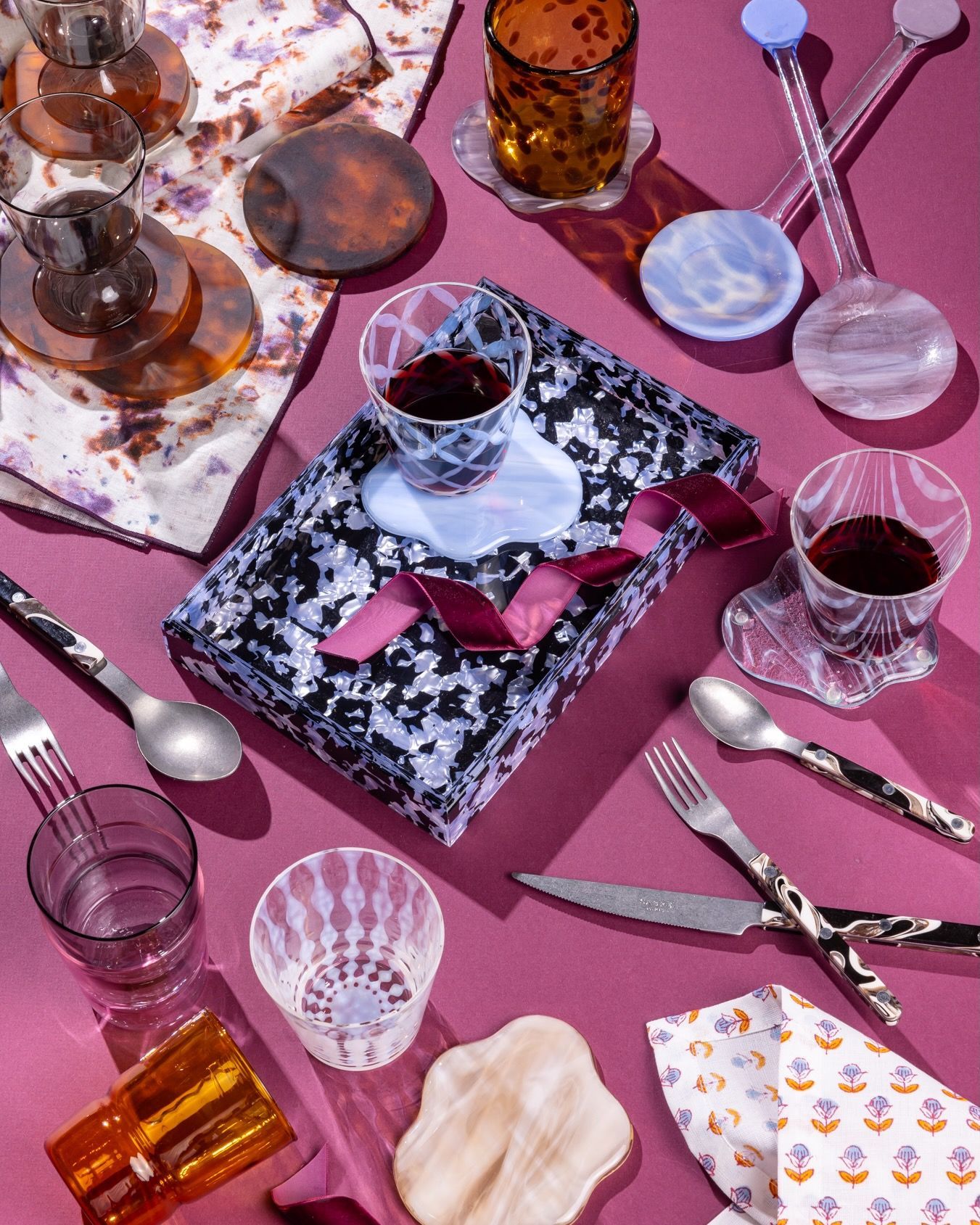 An artful arrangement of items with fun patterns and textures including glassware, an acrylic tray, sophisticated flatware and more.