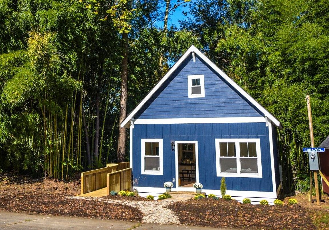 A newly built home that is painted blue with white trim and is surrounded by tall trees