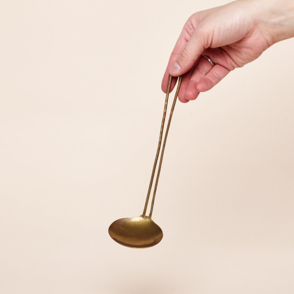 A hand holds a brass ladle that has a handle consisting of a long loop of brass