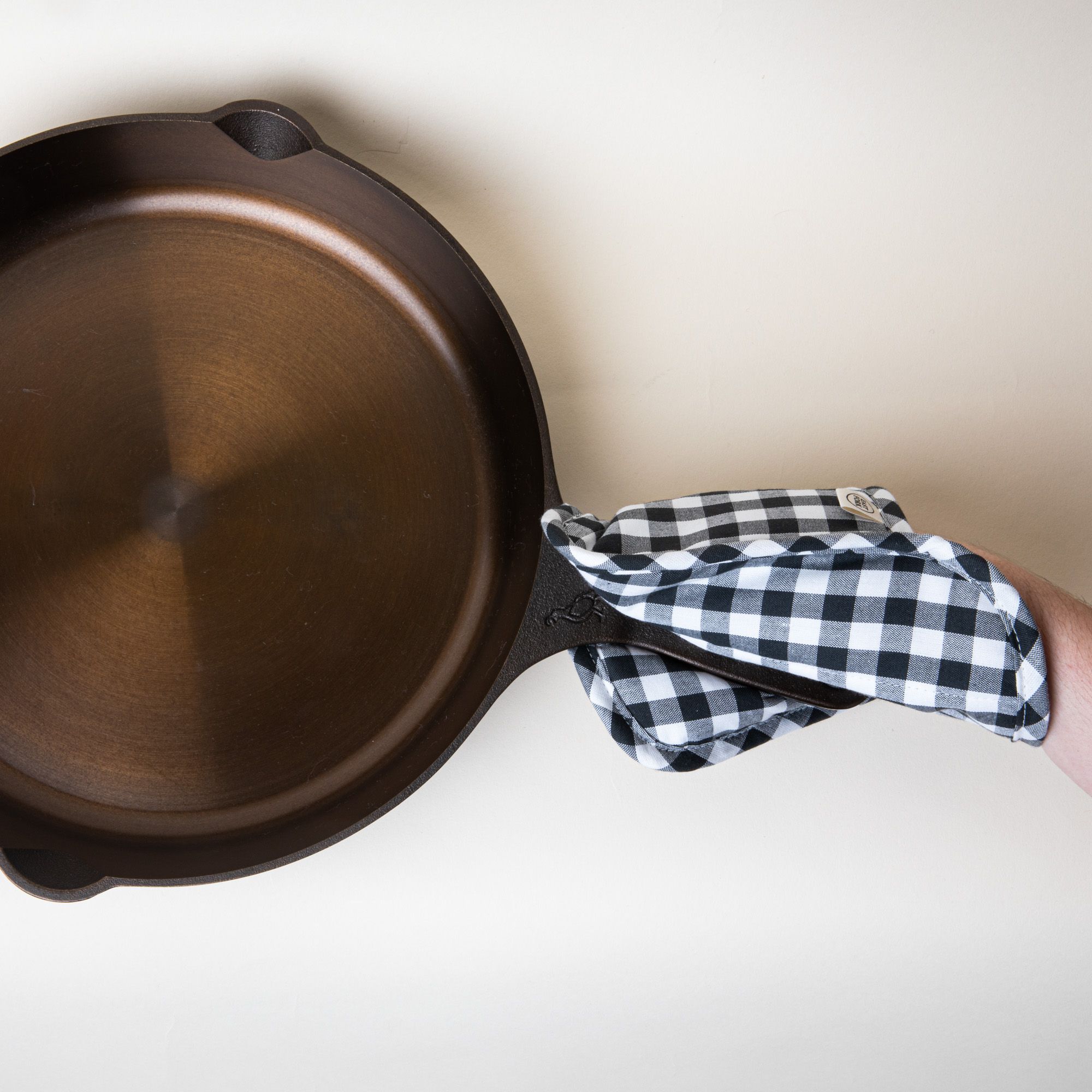 A skillet being held by a hand wearing a black and white gingham pot holder