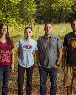 4 people stand outdoors smiling or looking directly at the camera.
