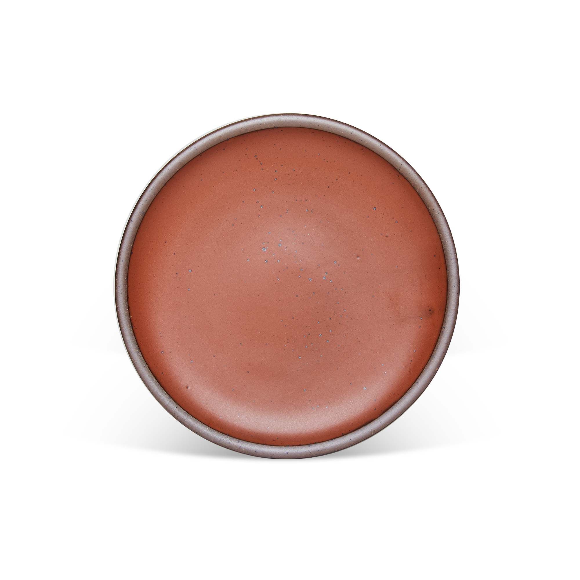 A dinner sized ceramic plate in a cool burnt terracotta color featuring iron speckles and an unglazed rim