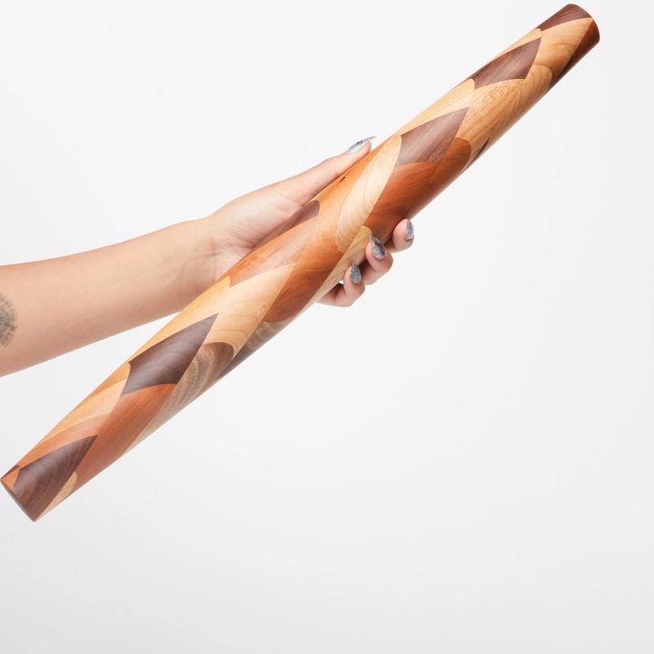 Hand holding a mixed wood rolling pin that tapers on each end