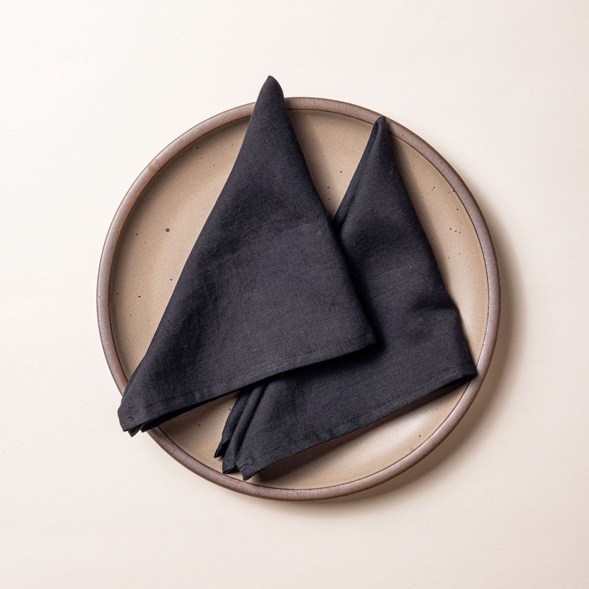 Two charcoal linen napkins folded into triangles on a warm brown ceramic plate.