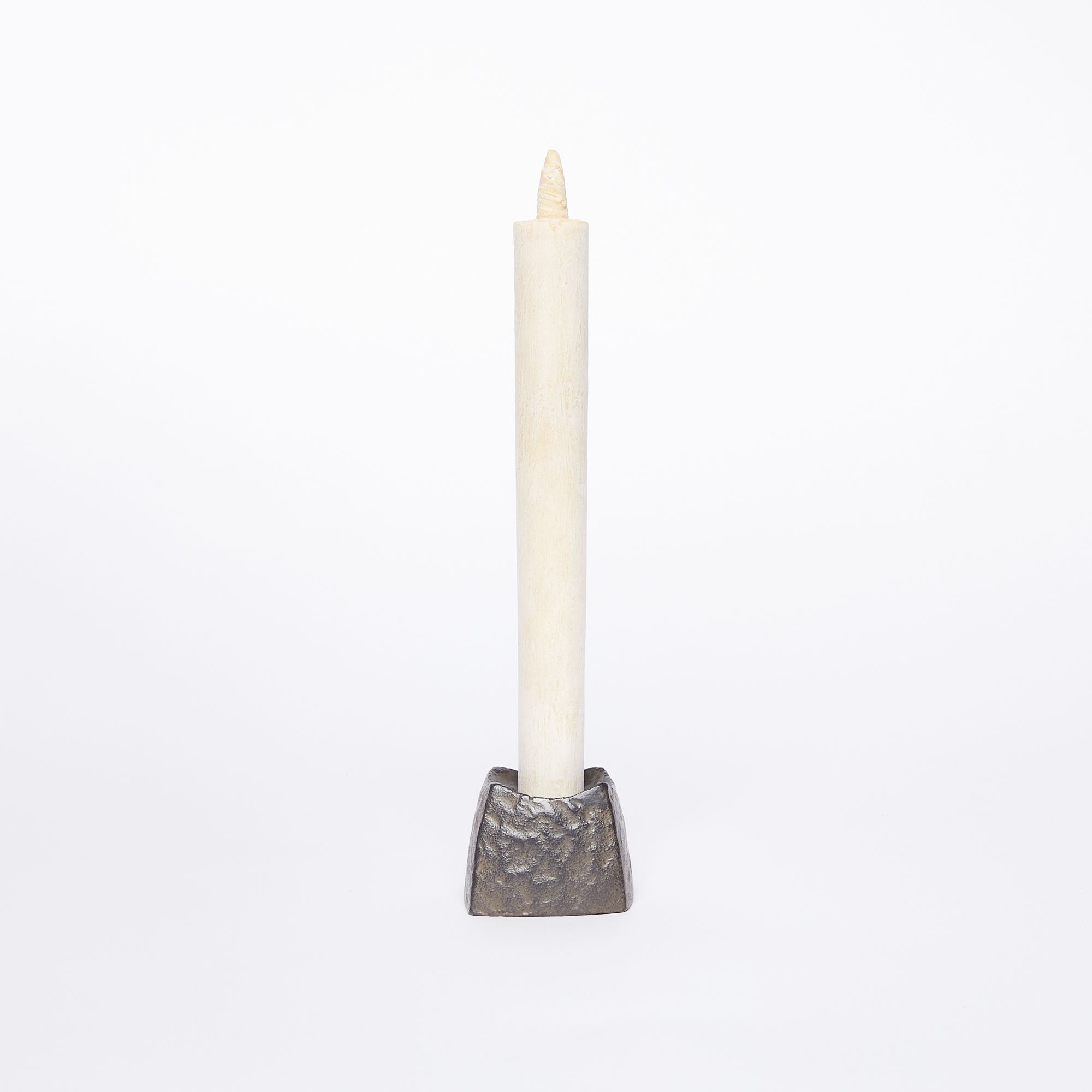 A small black square candle holder with a hammered metal outside holding a tall cream color candle