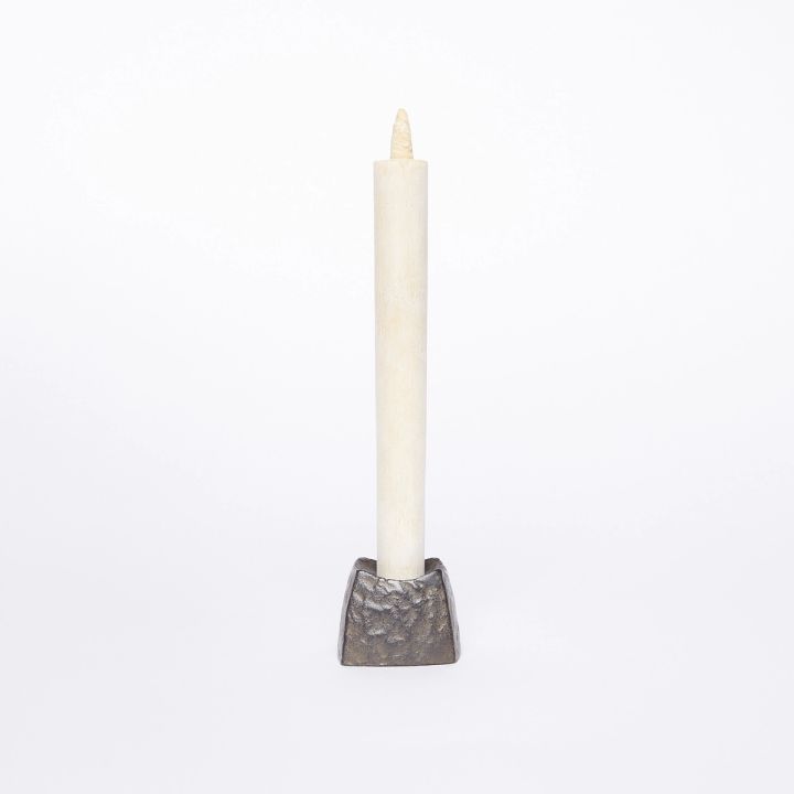 A small black square candle holder with a hammered metal outside holding a tall cream color candle