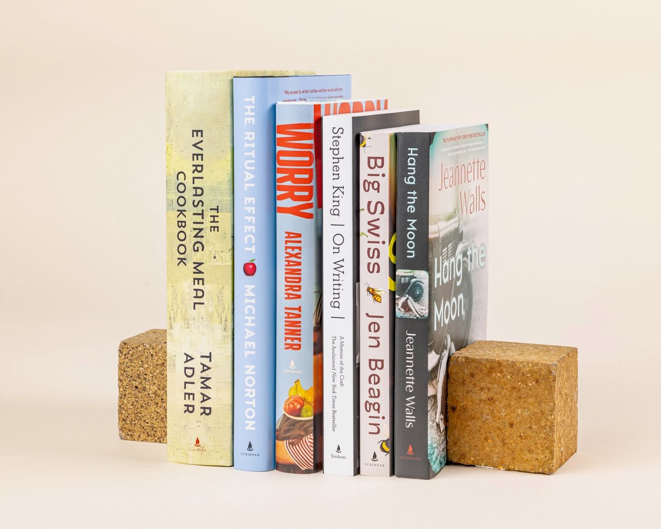 A stack of six books standing upright bookended by two brick blocks