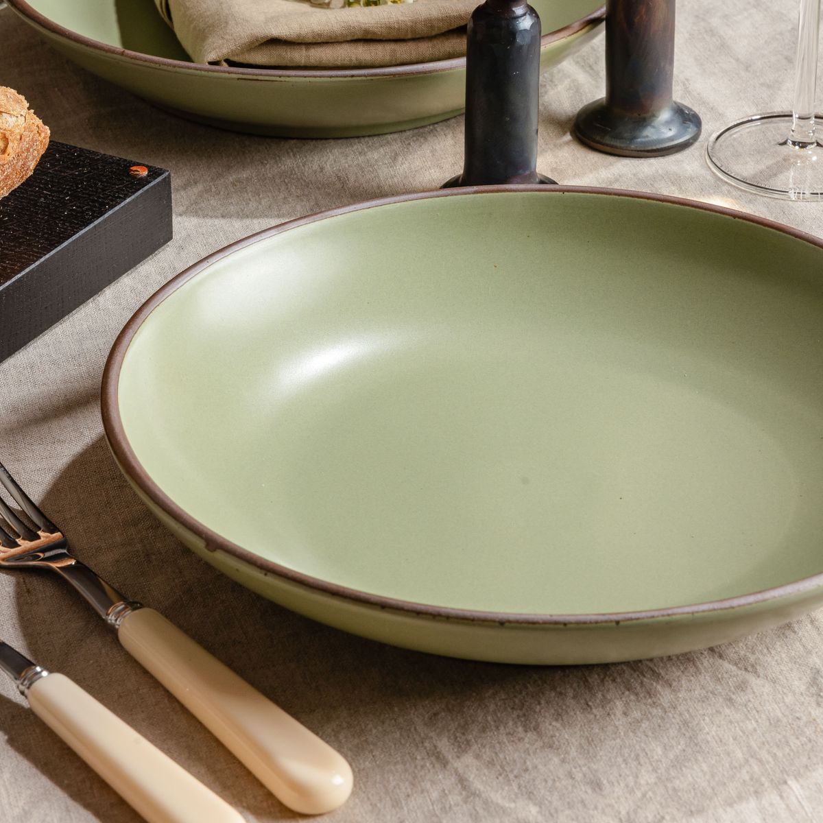 A large ceramic plate with a curved bowl edge in a calming sage green color featuring iron speckles and an unglazed rim.