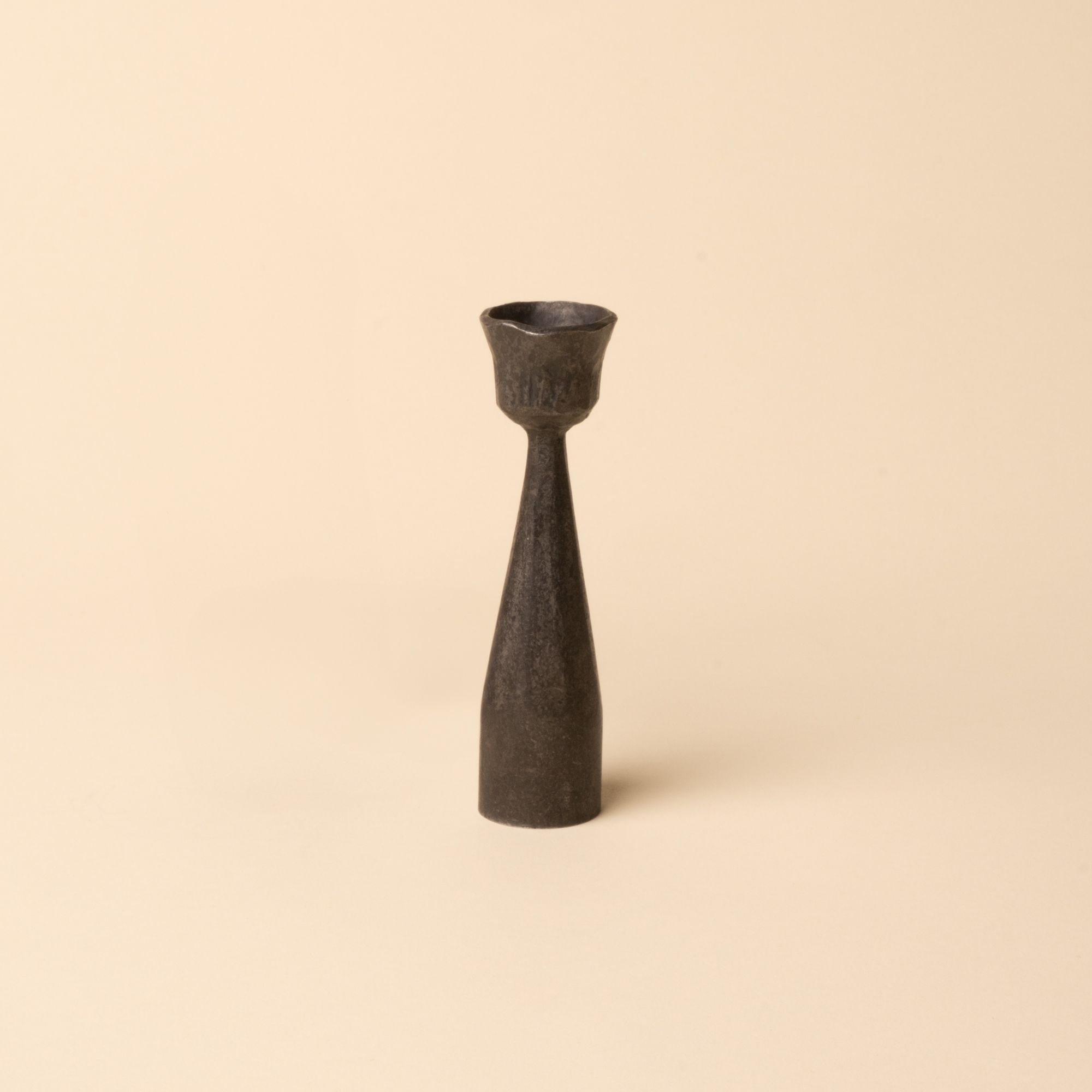 Forged iron candlestick holder with a narrow base and flared top, designed for taper candles, shown on a neutral beige background.