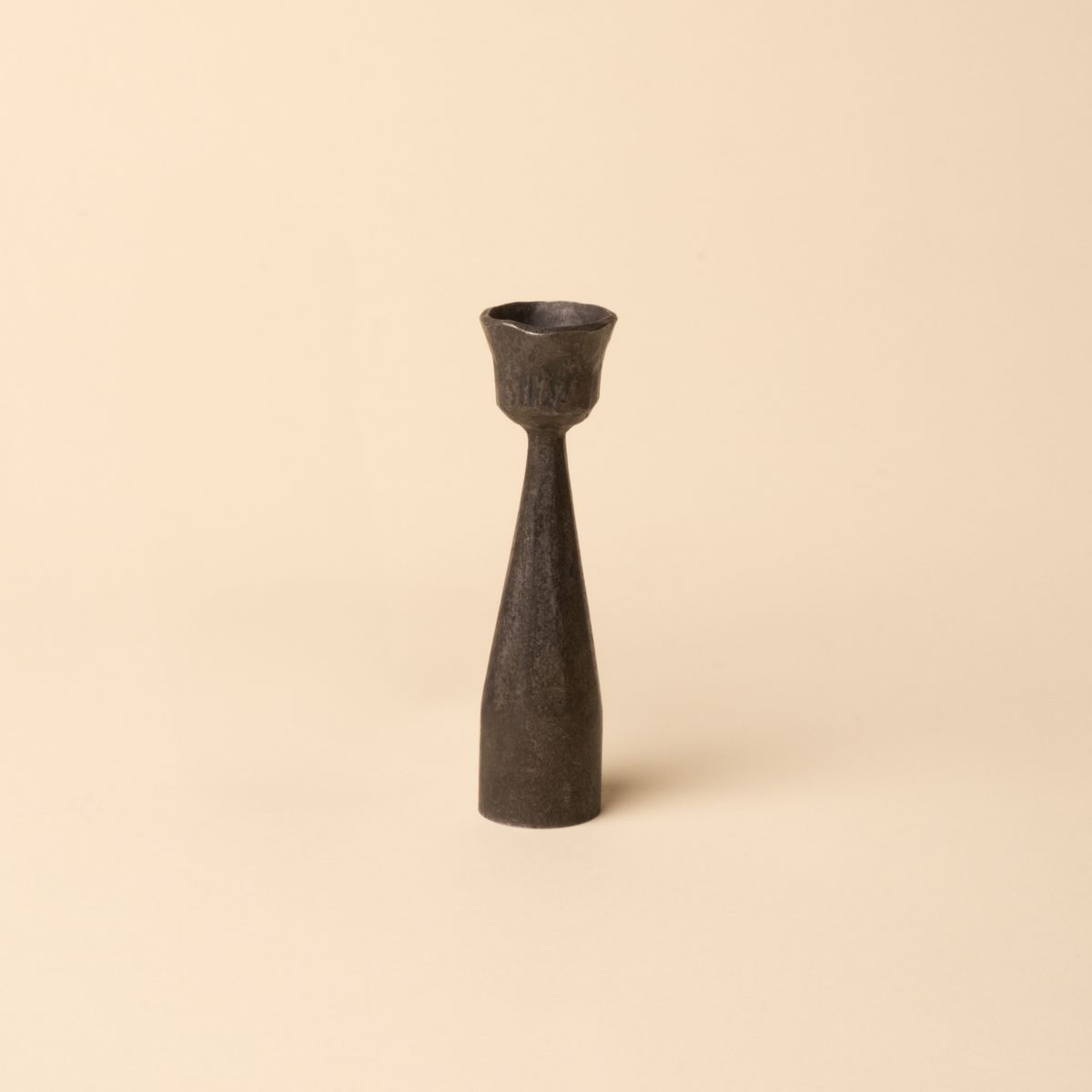 Forged iron candlestick holder with a narrow base and flared top, designed for taper candles, shown on a neutral beige background.