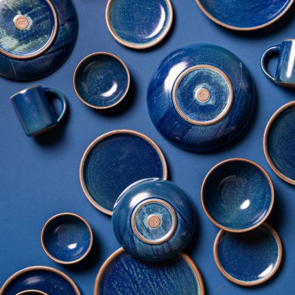 An artful flat lay of ceramic bowls and pots in a dappled deep blue glaze against a blue background