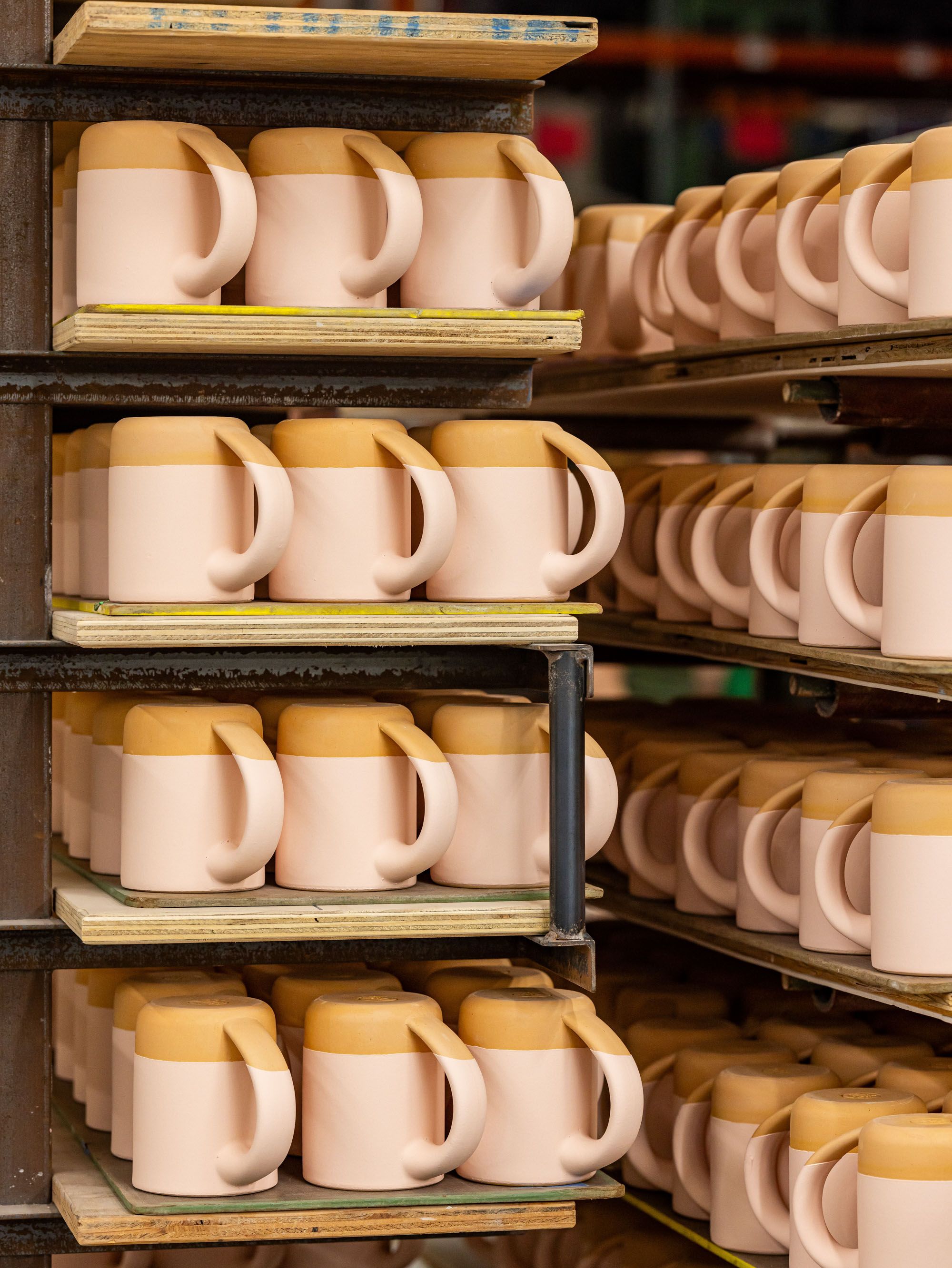 In a factory setting, there is a kiln cart filled with ceramic mugs that are waiting to be fired after glazing.