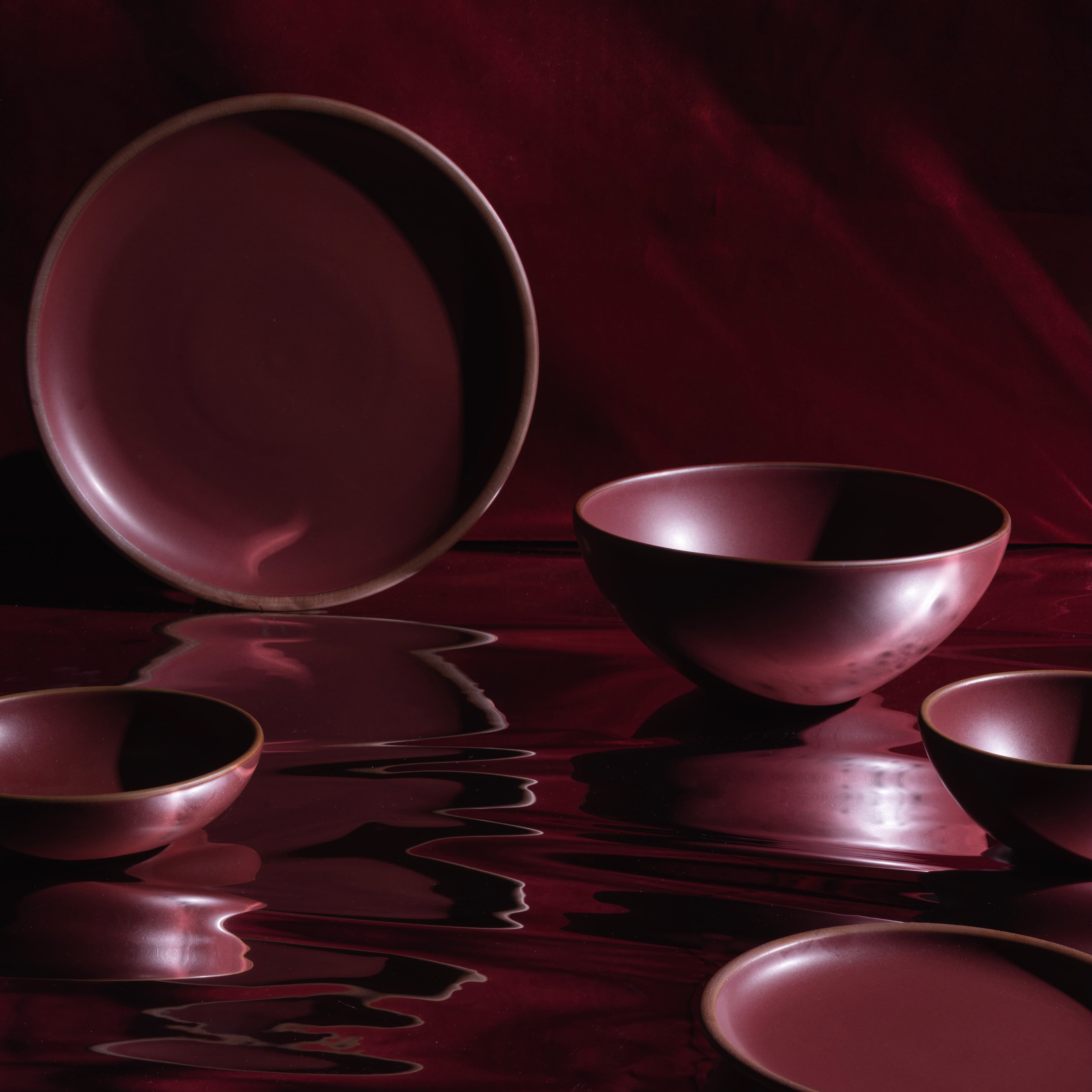 Ceramic plates and bowls in a plum color are in a moody setting with reflective light casting