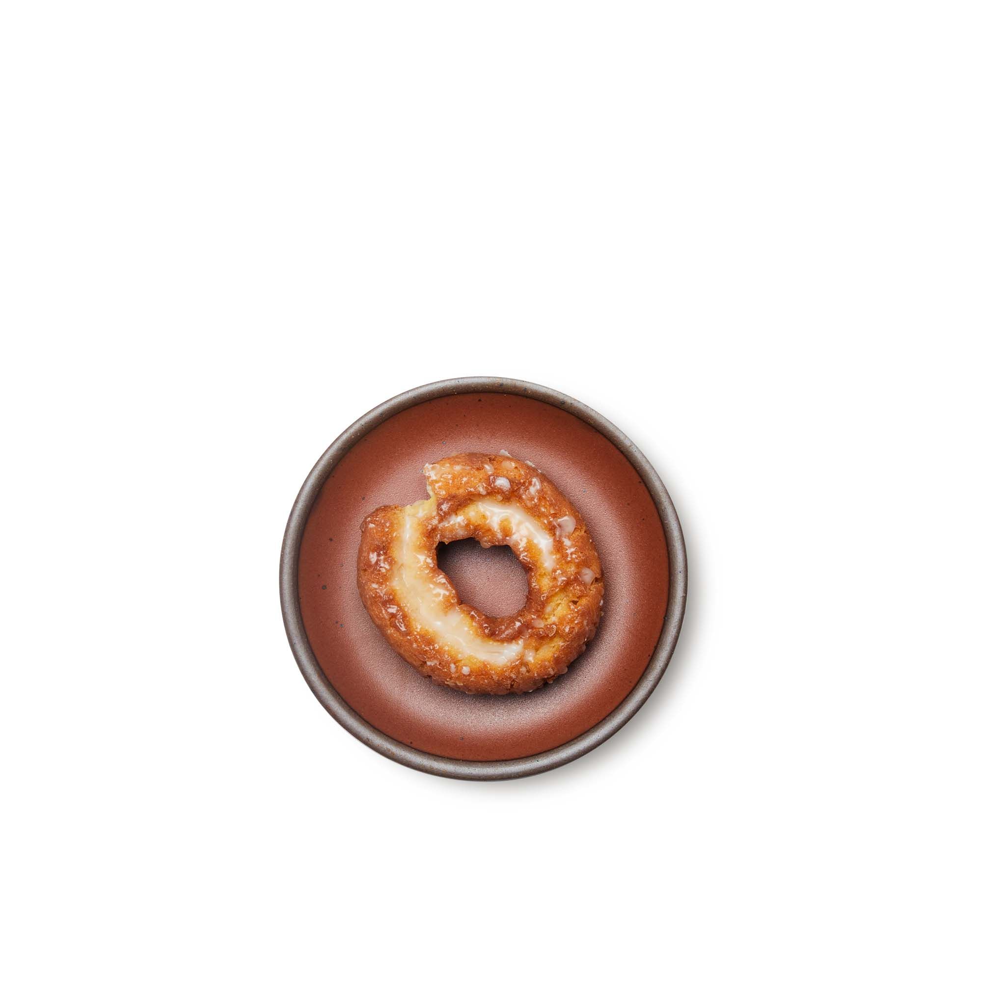 Glazed cake donut on a dessert sized ceramic plate in a cool burnt terracotta color featuring iron speckles and an unglazed rim.