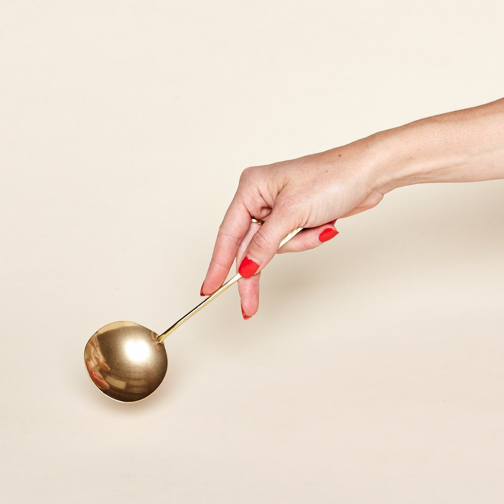 A brass serving spoon with a long thin handle is held by a hand.