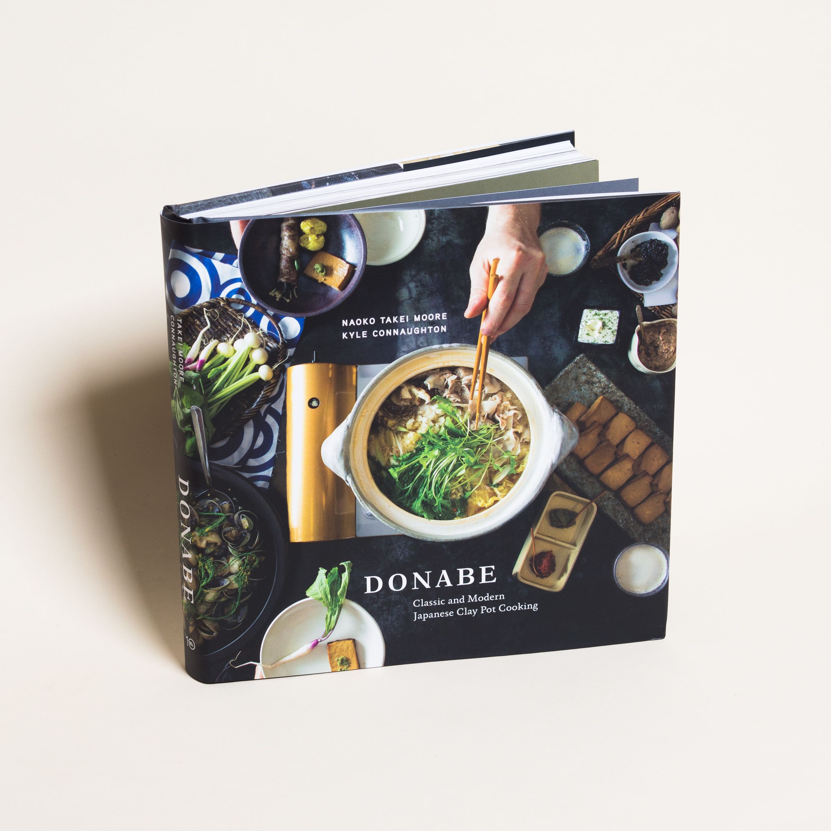 Front cover of "Donabe," showing a clay pot filled with soup and greens surrounded by bowls and ingredients, a hand reaching in with chopsticks