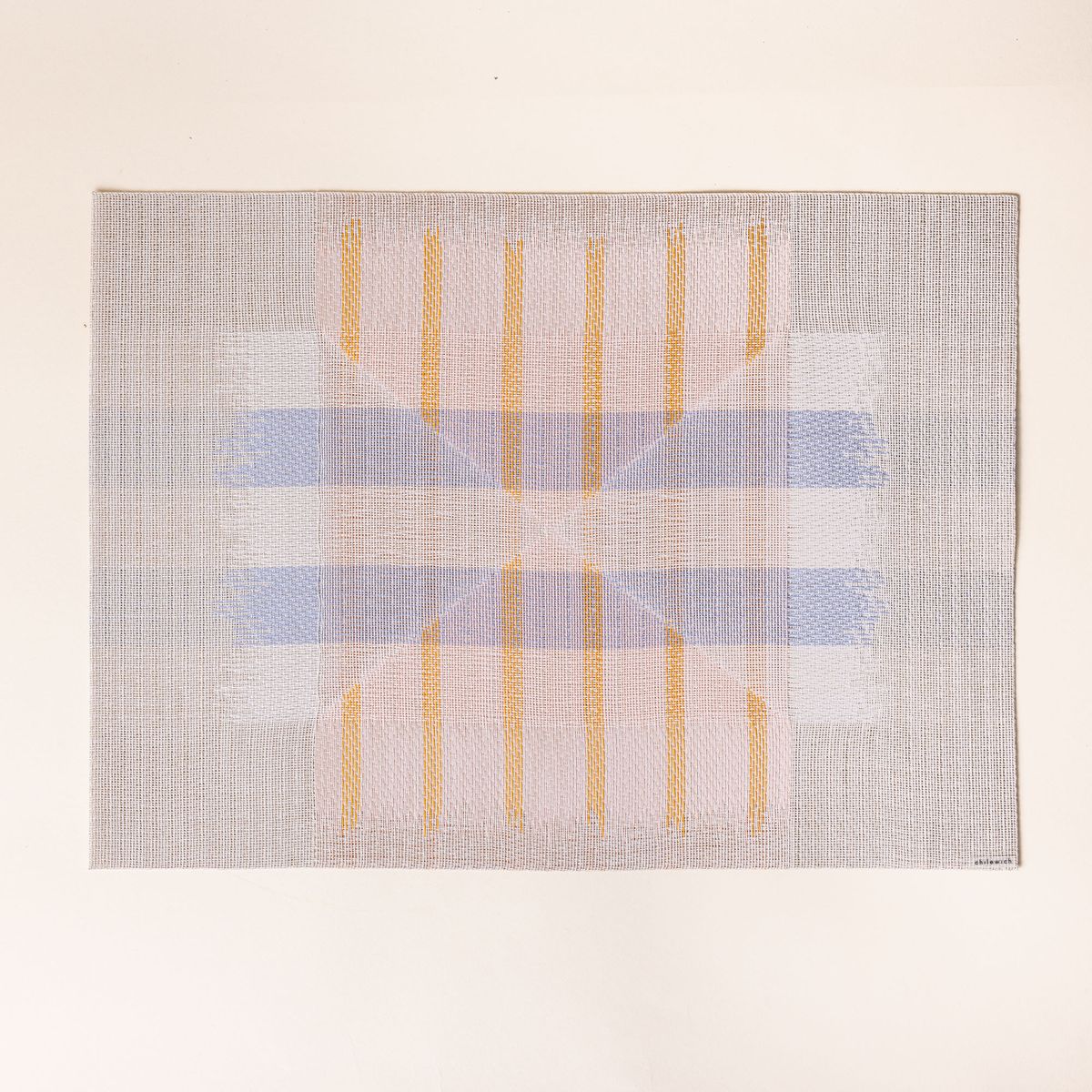 A placemat with a soft artful geometric design featuring neutral, orange, white, and blue colors